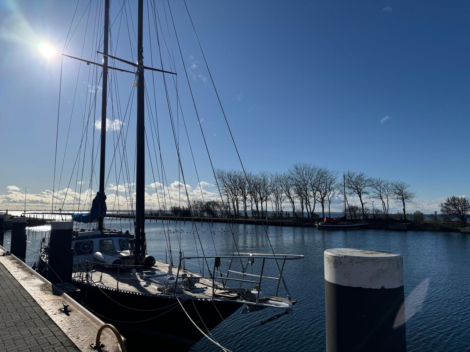 Segelboot liegt im Hafen, Sonne scheint, Wasser spiegelt den Himmel.