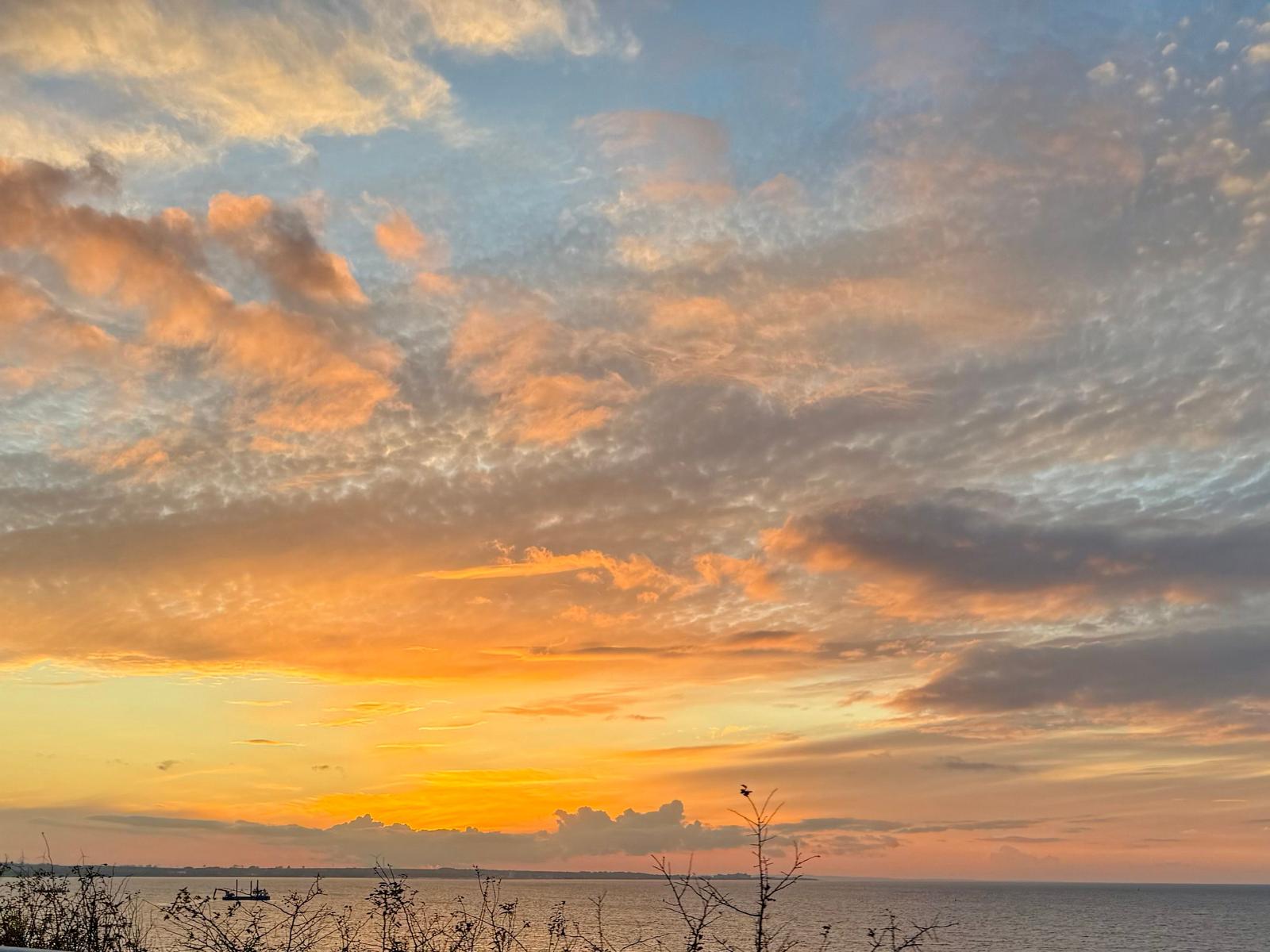 Sonnenuntergang über dem Wasser mit orangefarbenen Wolken am Horizont.