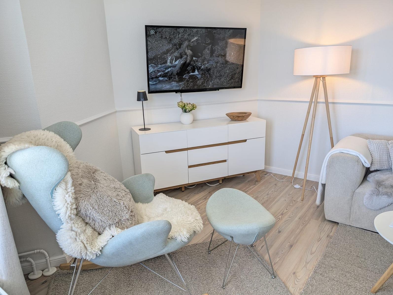 Wohnzimmer mit Fernseher, Sessel und Stehlampe.