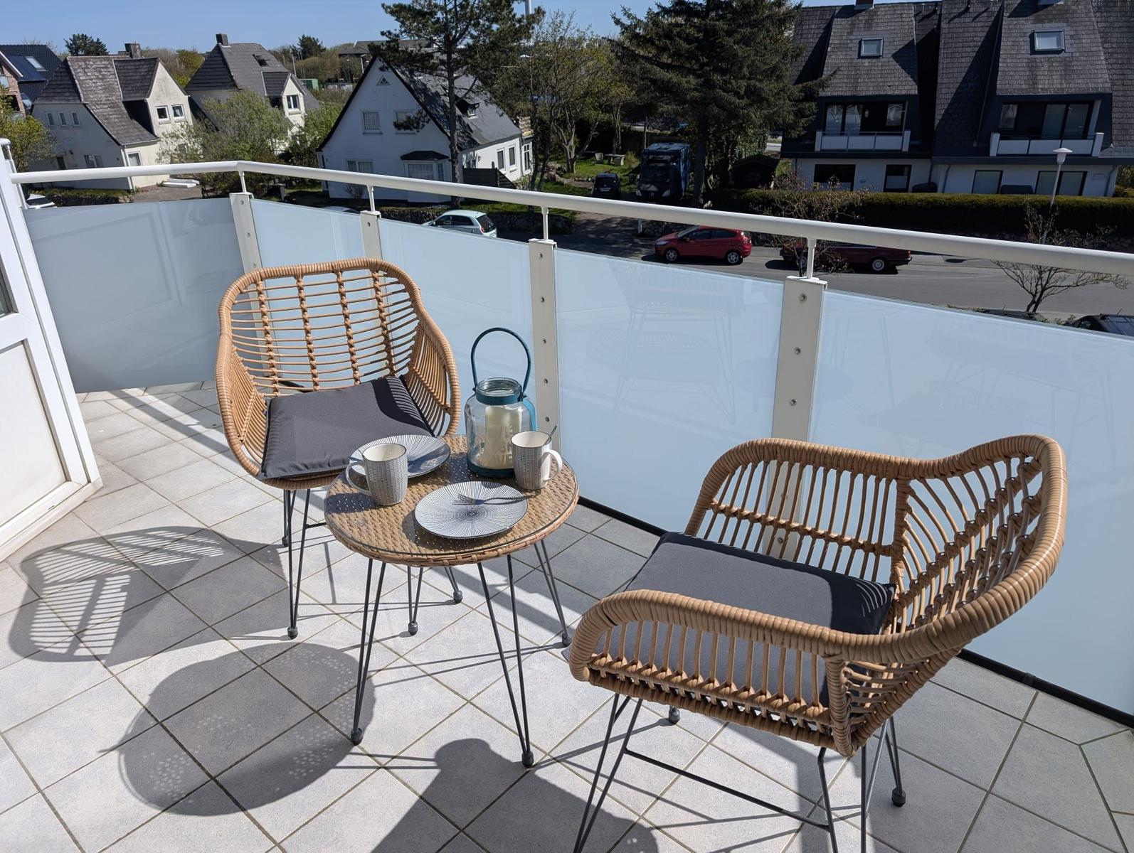 Terrasse mit zwei Stühlen und Tisch. Blick auf Wohngebiet mit Häusern und Bäumen.