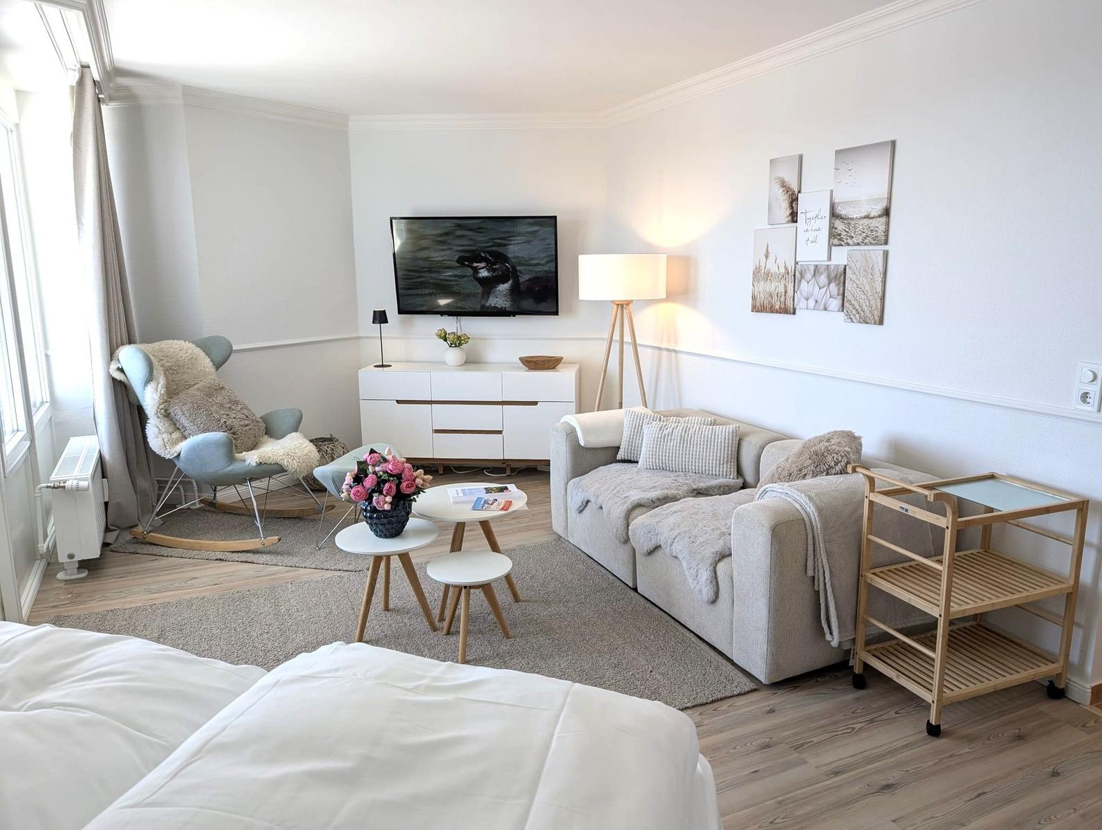 Wohnbereich mit Sofa, Fernseher und Schaukelstuhl. Holzboden und Wandbilder.