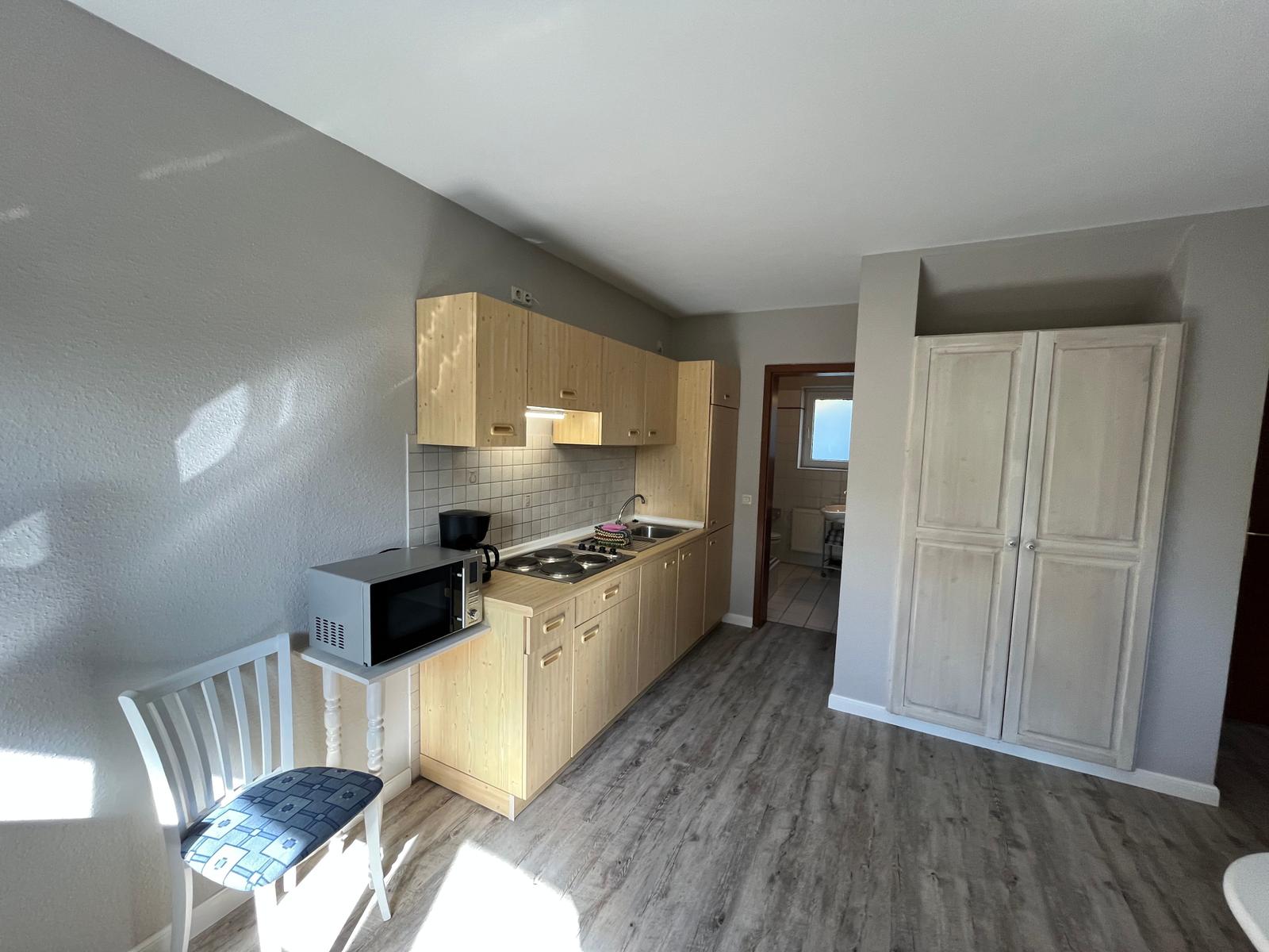 Küche mit Holzschränken, Mikrowelle und Stuhl.
