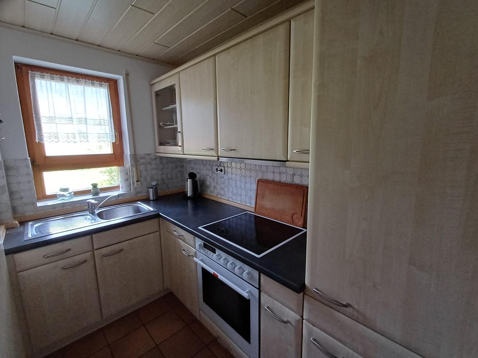 Küche mit Holzschränken, Induktionskochfeld und Fenster mit Vorhang.