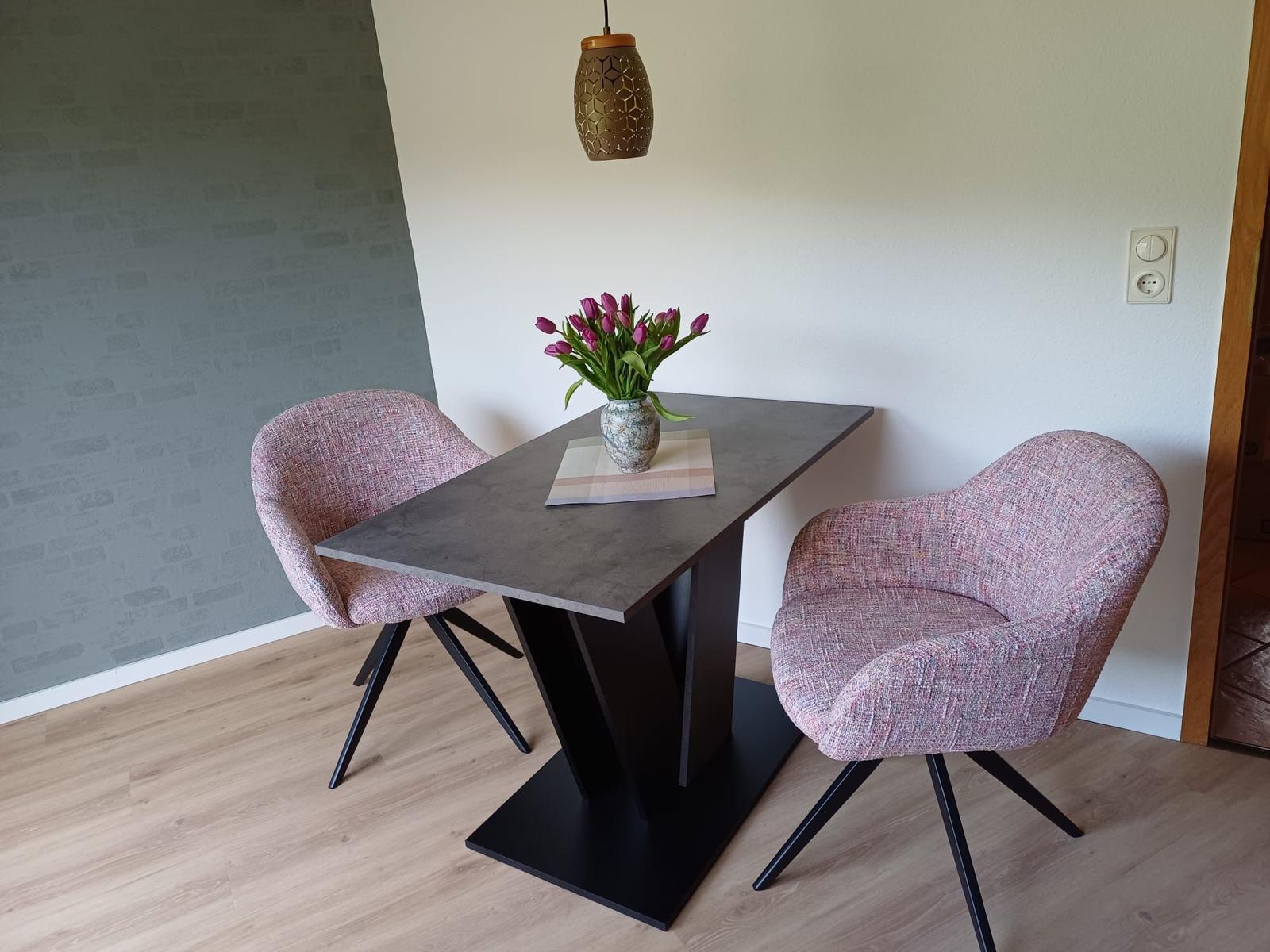 Essbereich mit Tisch, zwei Stühlen und Blumenarrangement.