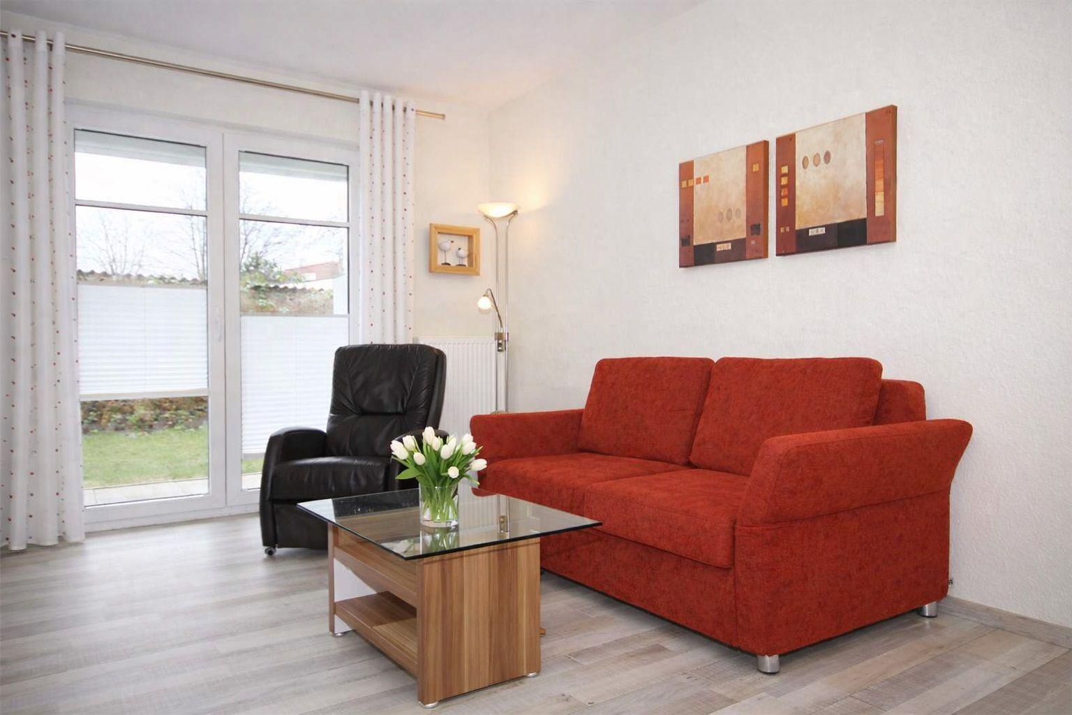 Ein Wohnzimmer mit rotem Sofa, Glas-Tisch und schwarzer Ledercouch. An der Wand hängen zwei Bilder.
