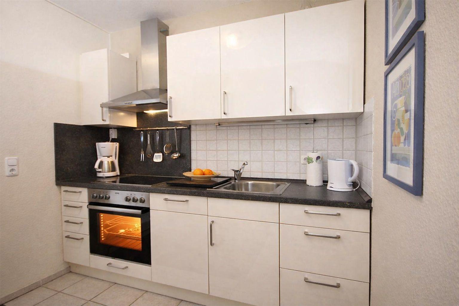 Küche mit weißen Schränken, Edelstahlspüle und Backofen mit eingeschaltetem Licht.