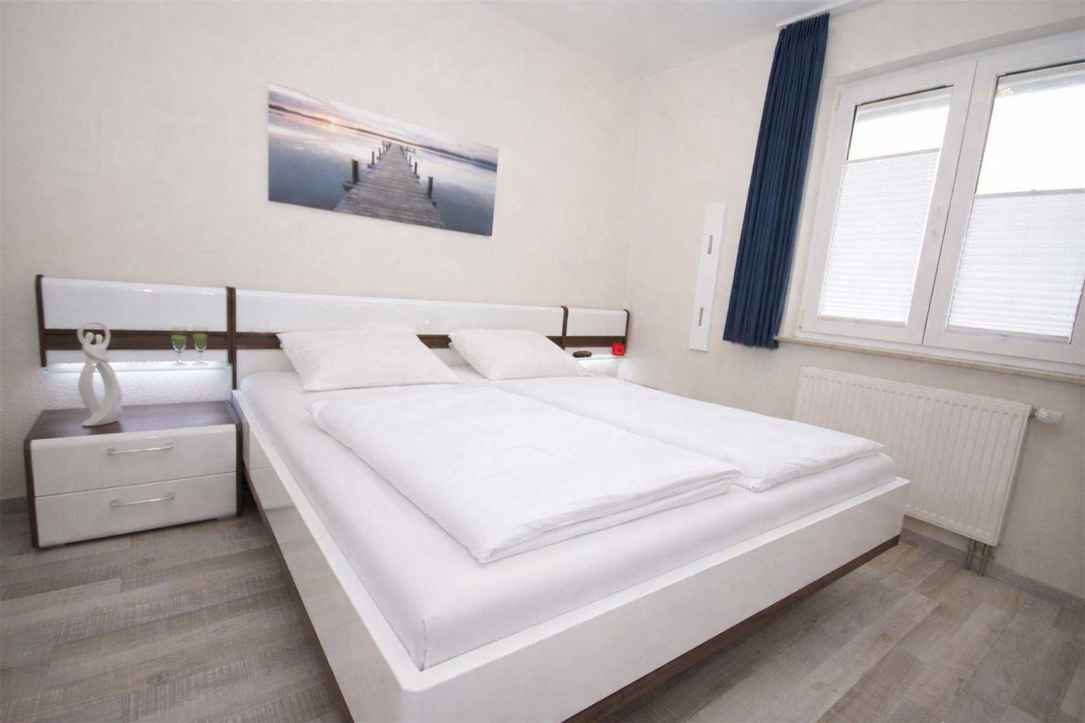 Schlafzimmer mit Doppelbett, Nachttisch und Fenster mit Jalousie.