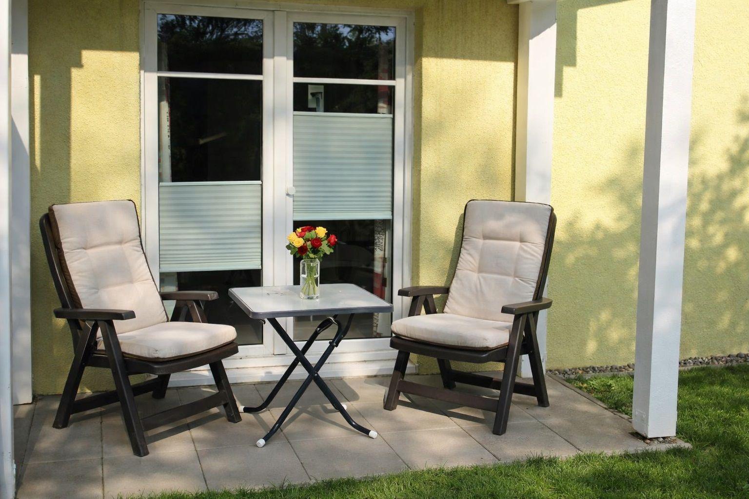 Zwei Stühle und ein Tisch vor einer Glastür mit Blumen darauf.