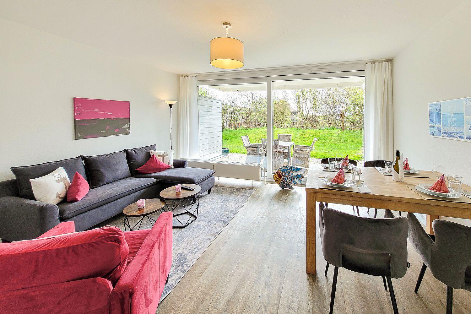 Wohn- und Essbereich mit Blick auf Garten. Sofa, Tisch und Stühle sind sichtbar.
