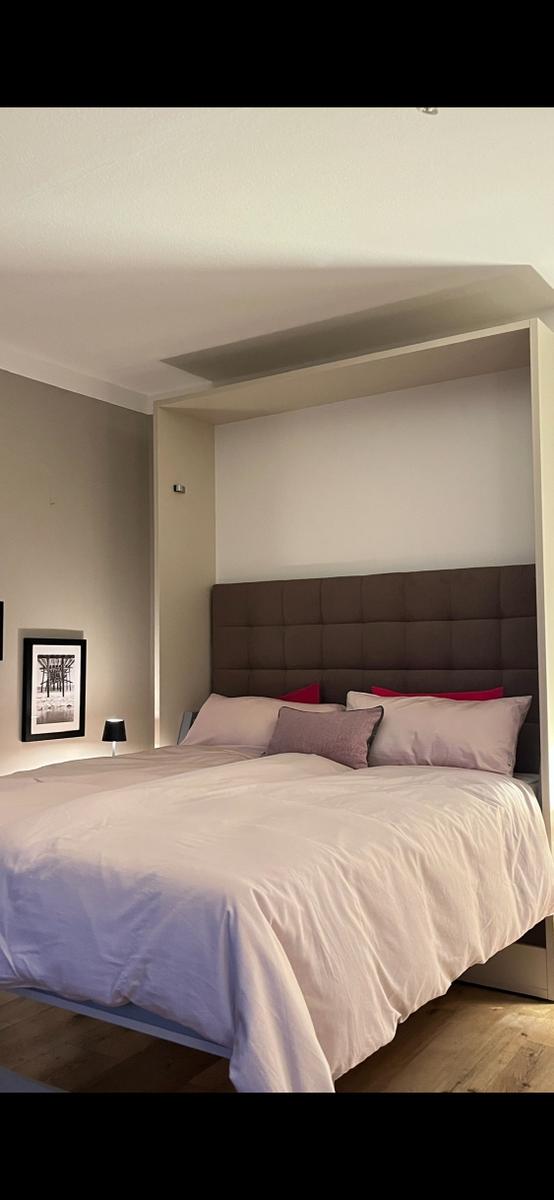Schlafzimmer mit Bett, Kopfteil und Wandbeleuchtung