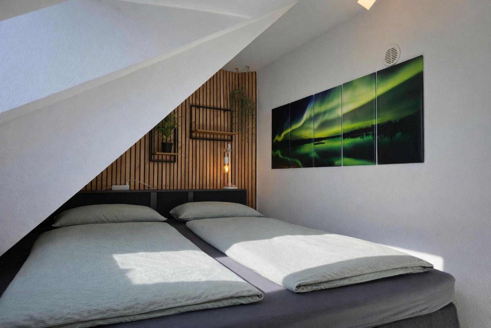 Schlafzimmer mit Doppelbett, Holzwand und Nordlicht-Bild an der Wand.