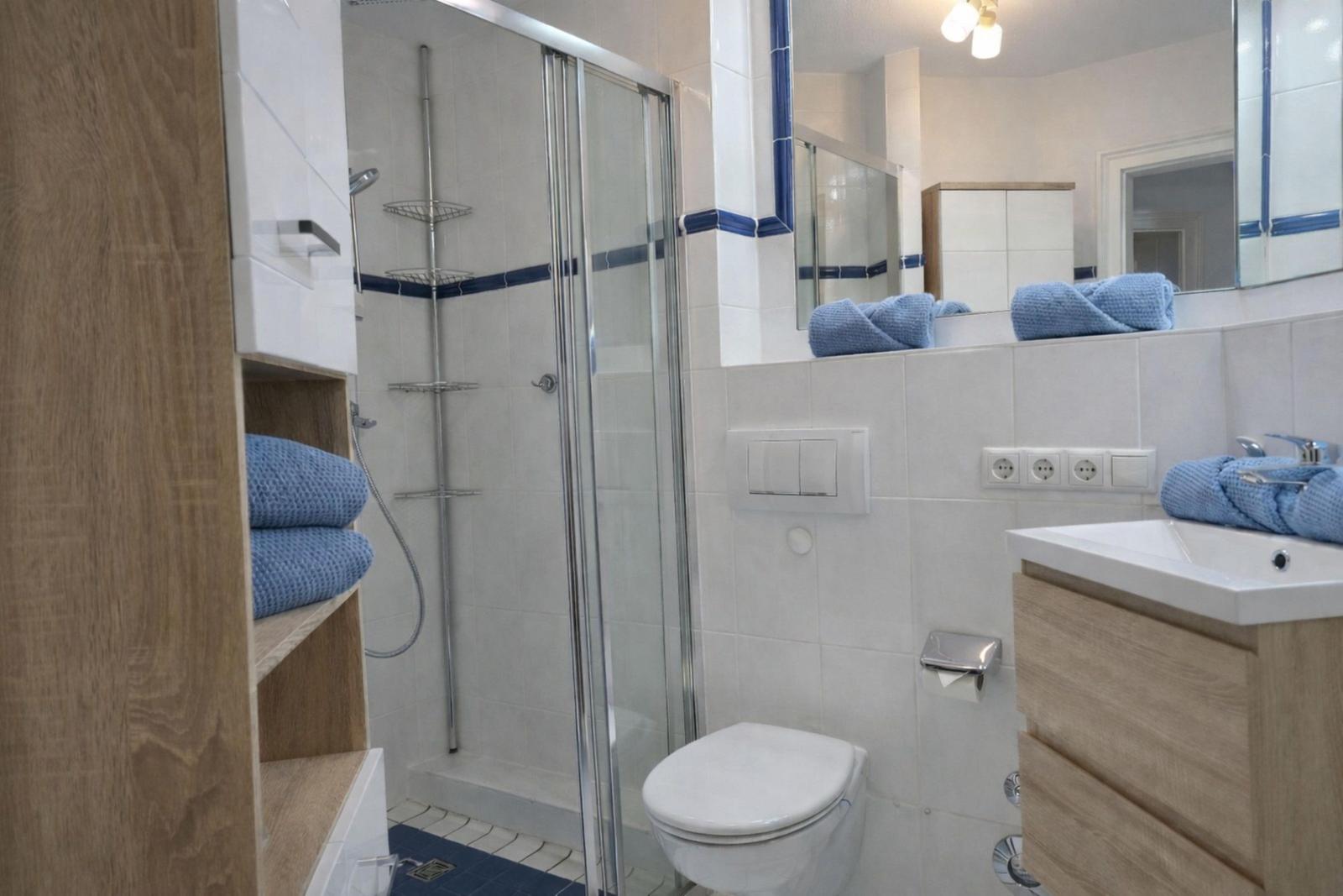 Badezimmer mit Dusche, Toilette und Waschbecken mit blauen Handtüchern.