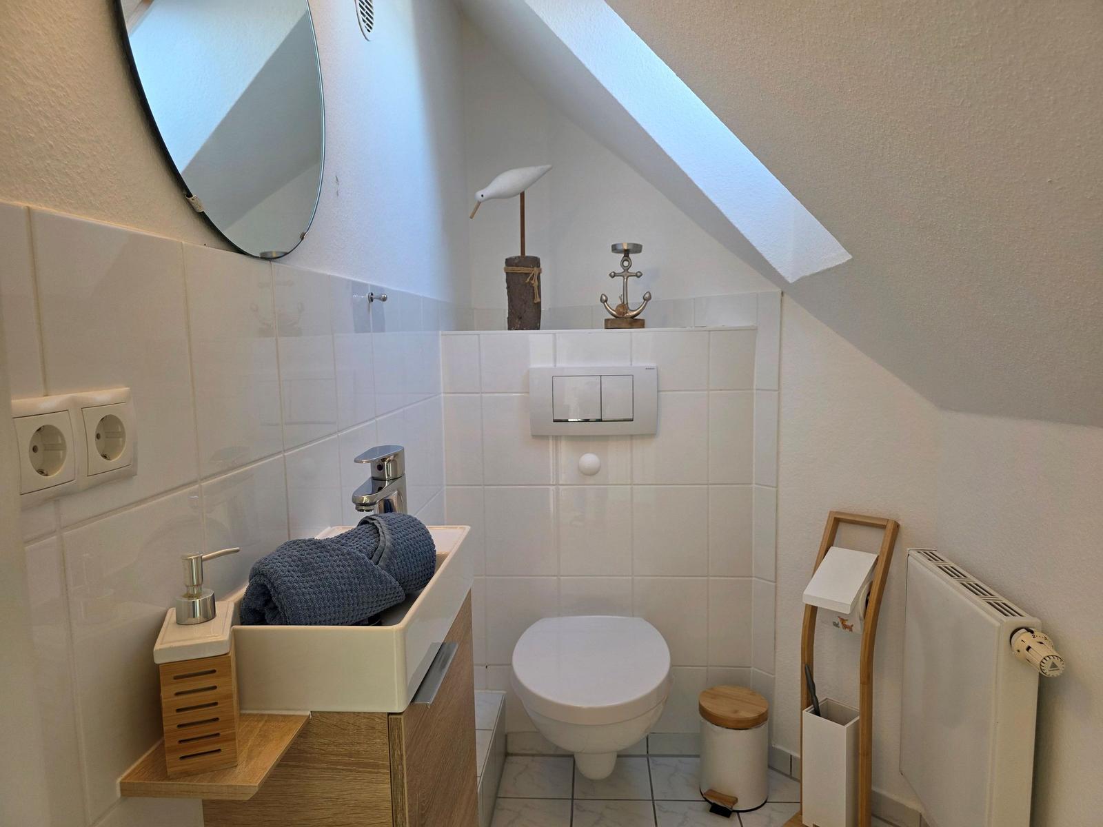 Badezimmer mit Toilette, Waschbecken und Spiegel unter Dachschrägen.