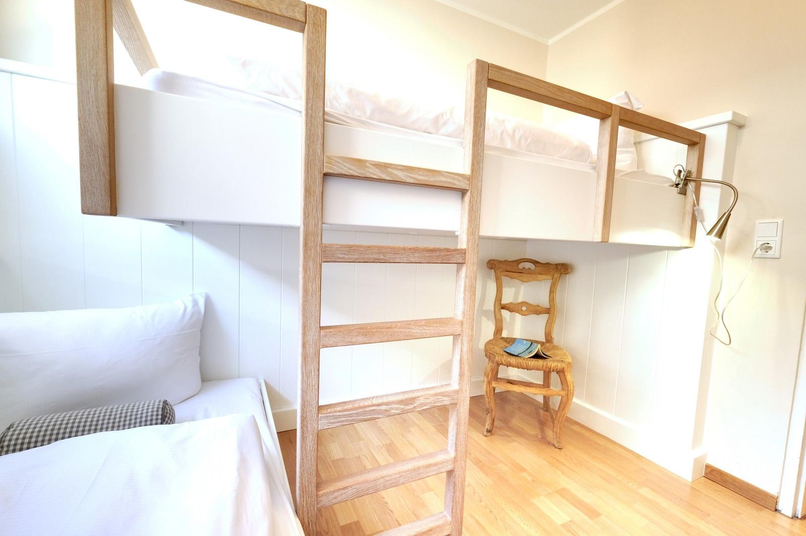Upper and lower bunk beds with wooden ladder and chair.