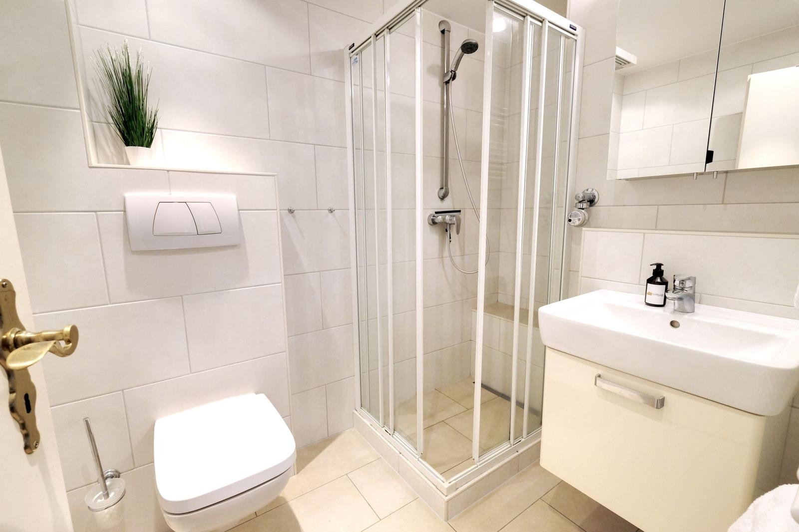 Bathroom with shower, sink and toilet. White tiles and mirror.