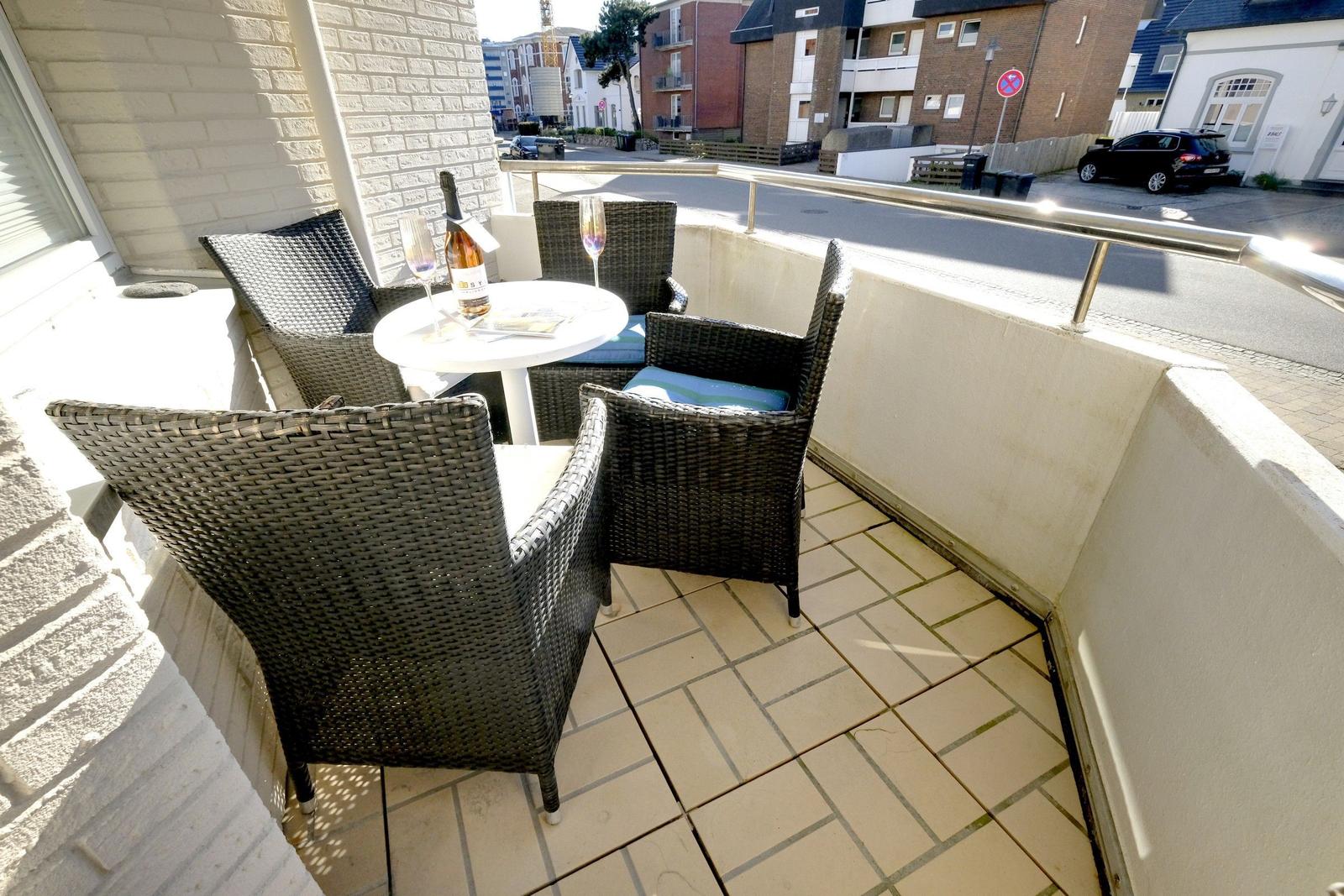 Balcony with table and four chairs, bottle and glasses on it.