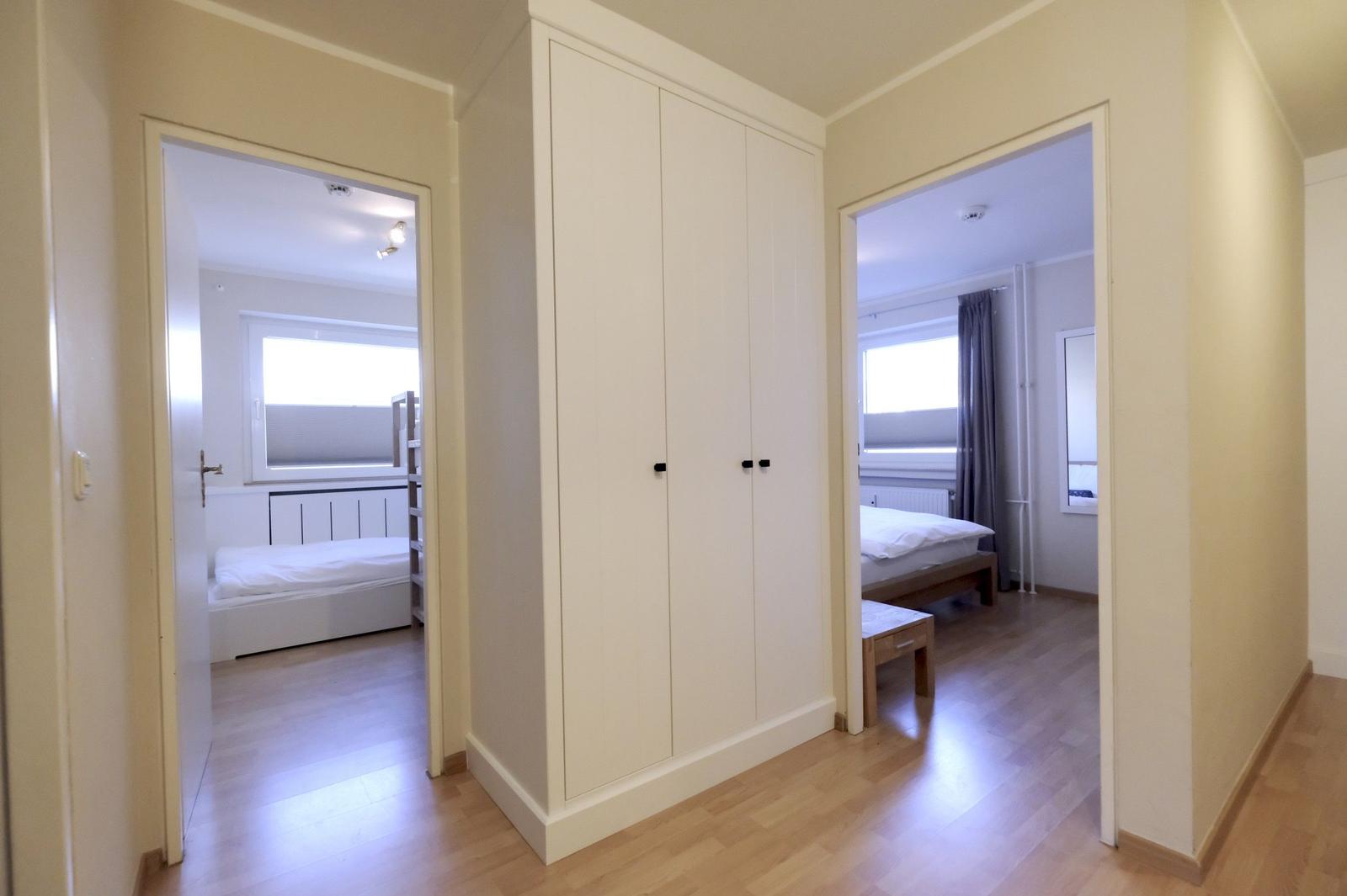 Two bedrooms with beds and windows. Between them stands a white wardrobe.