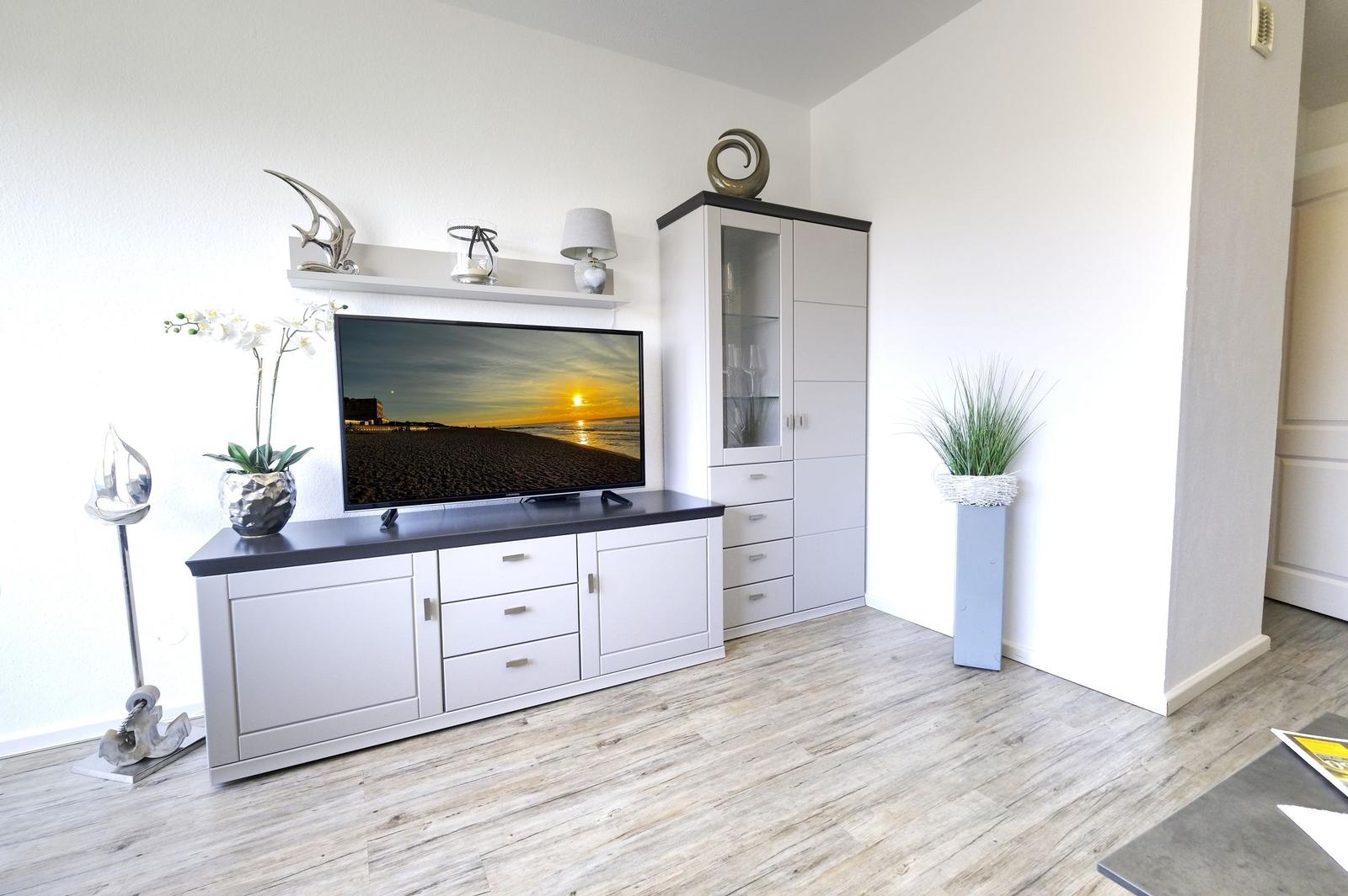 Wohnzimmer mit Fernseher, Schrank und Pflanzen auf Holzboden.