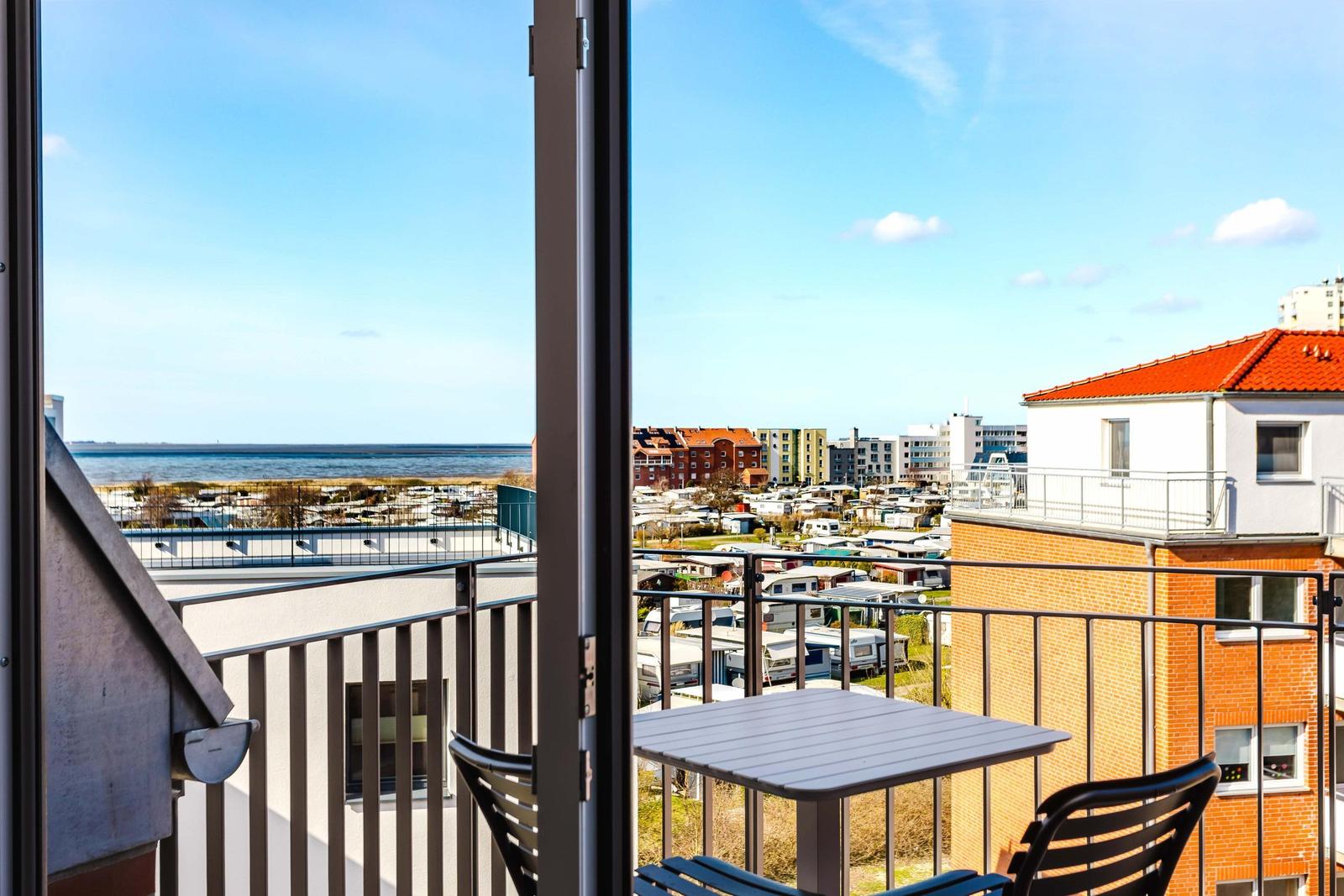 Balkon mit Tisch und Stühlen. Blick auf Meer und Wohngebiet.