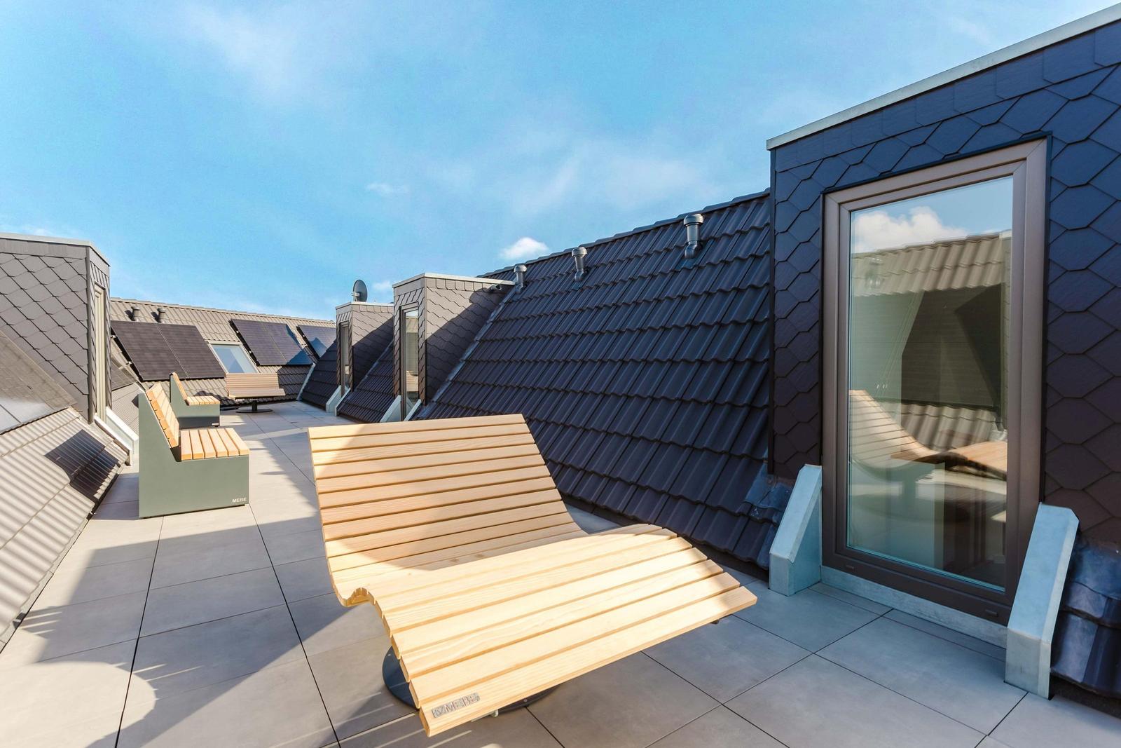 Dachterrasse mit Holzliege und Blick auf Dächer.