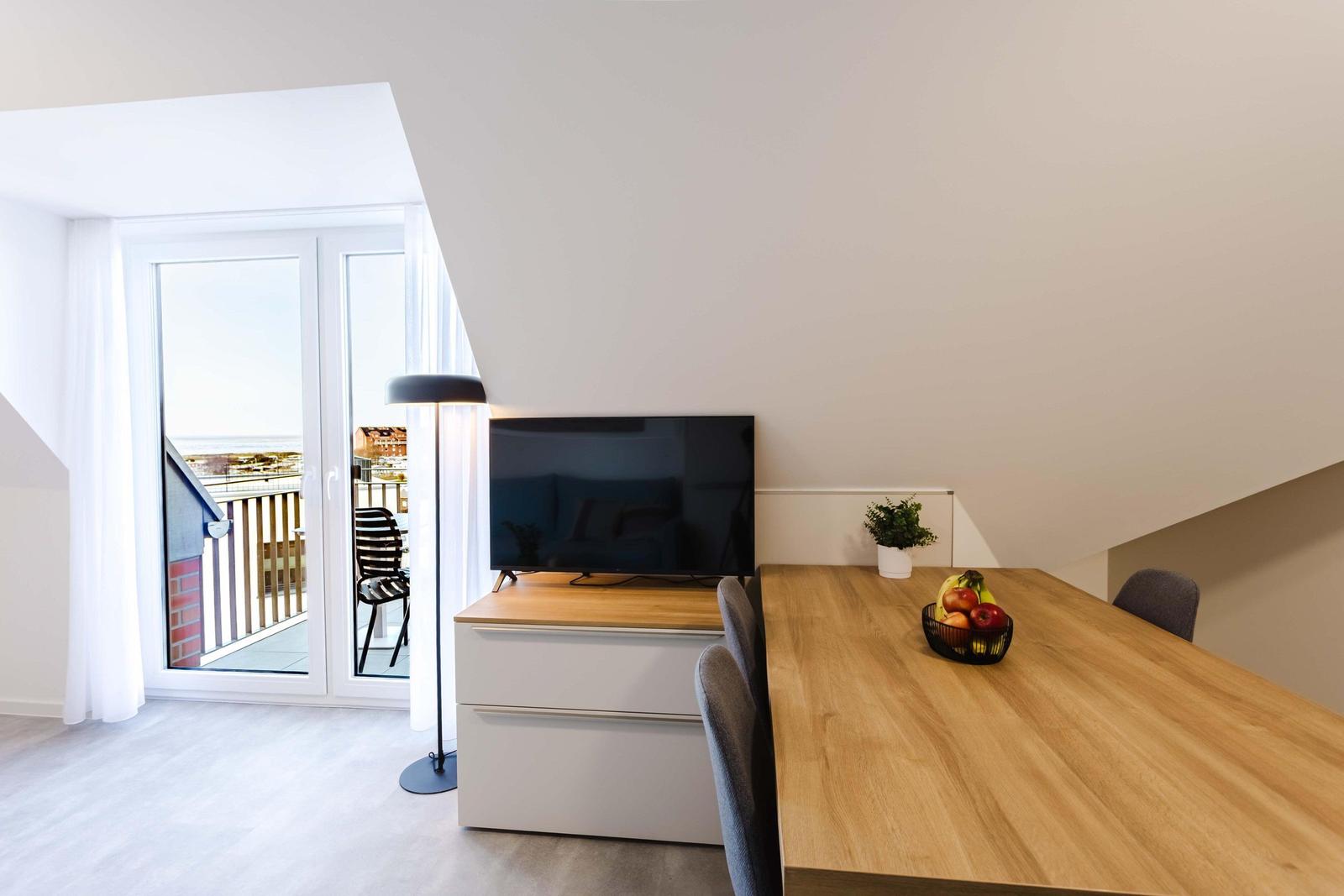 Ein Raum mit Esstisch, Fernseher und Balkontür mit Meerblick.