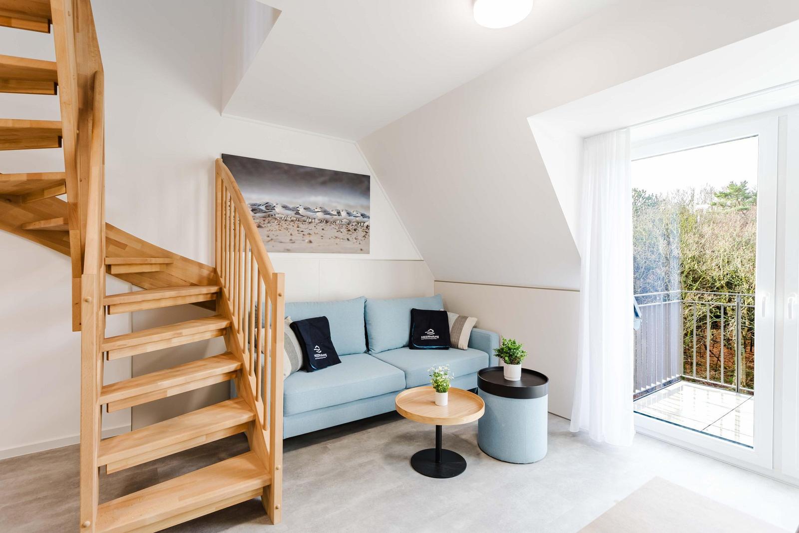 Wohnbereich mit Holztreppe, Sofa und Balkonzugang.