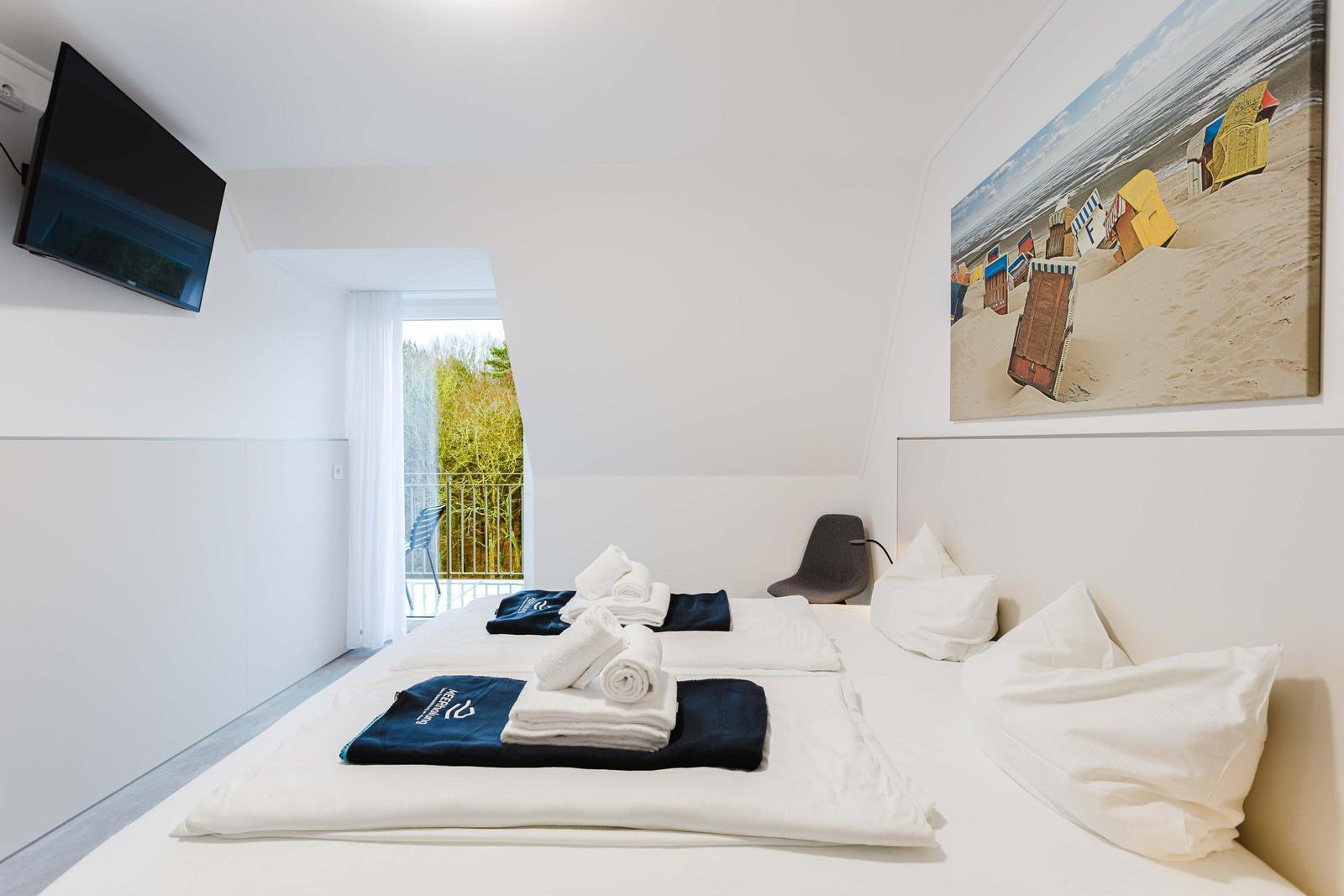Schlafzimmer mit Doppelbett, TV und Balkon. Wandbild zeigt Strandkörbe.