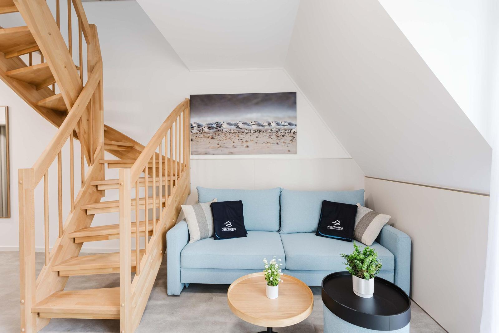 Ein Wohnbereich mit blauem Sofa, Holztreppe und Wandbild.