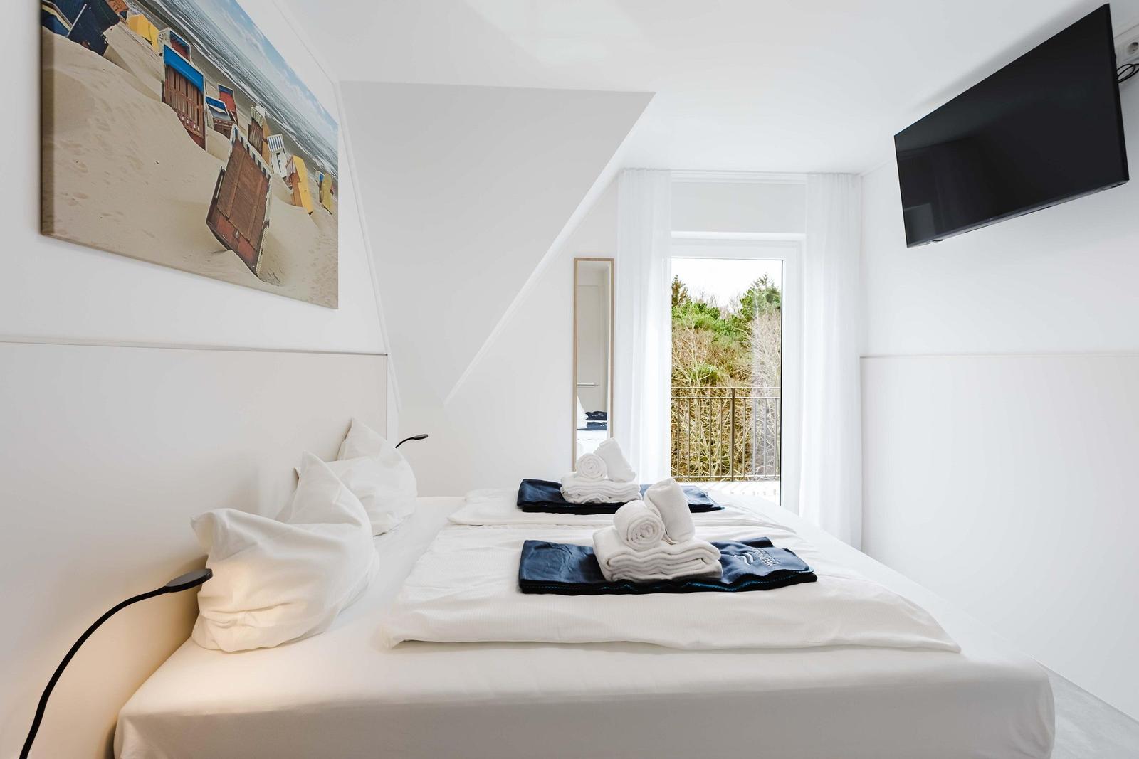 Schlafzimmer mit Doppelbett, TV und Balkonansicht. Wandbild zeigt Strand.
