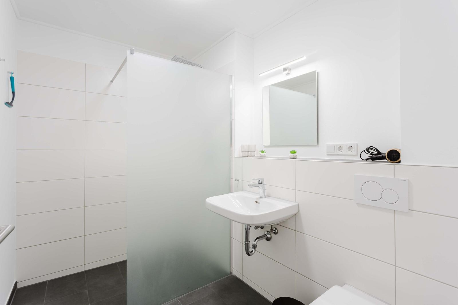 Badezimmer mit Dusche, Waschbecken und Spiegel. Fliesen und graue Bodenfliesen.