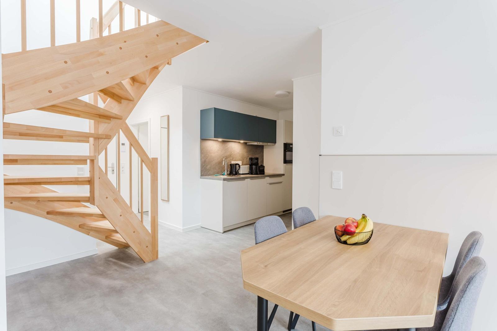 Essbereich mit Tisch und Stühlen. Hintergrund: Küche und Holztreppe.
