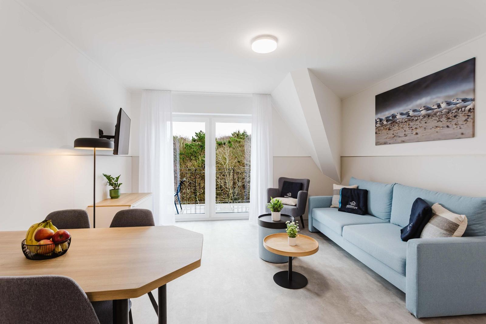 Wohnbereich mit Sofa, Esstisch und Balkon mit Blick auf Bäume.