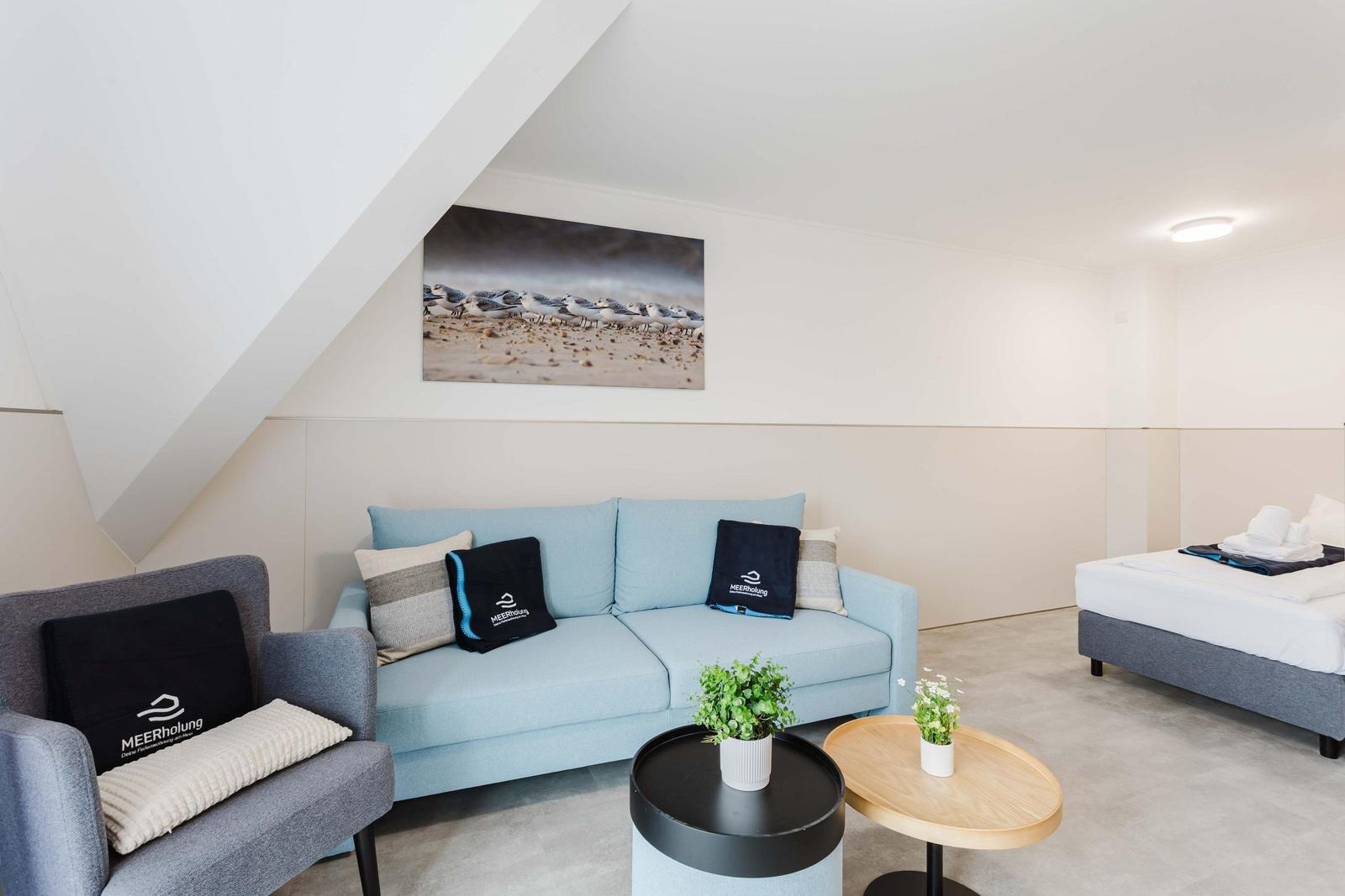 Wohnbereich mit Sofa, Sessel und Bett unter schrägem Dach
