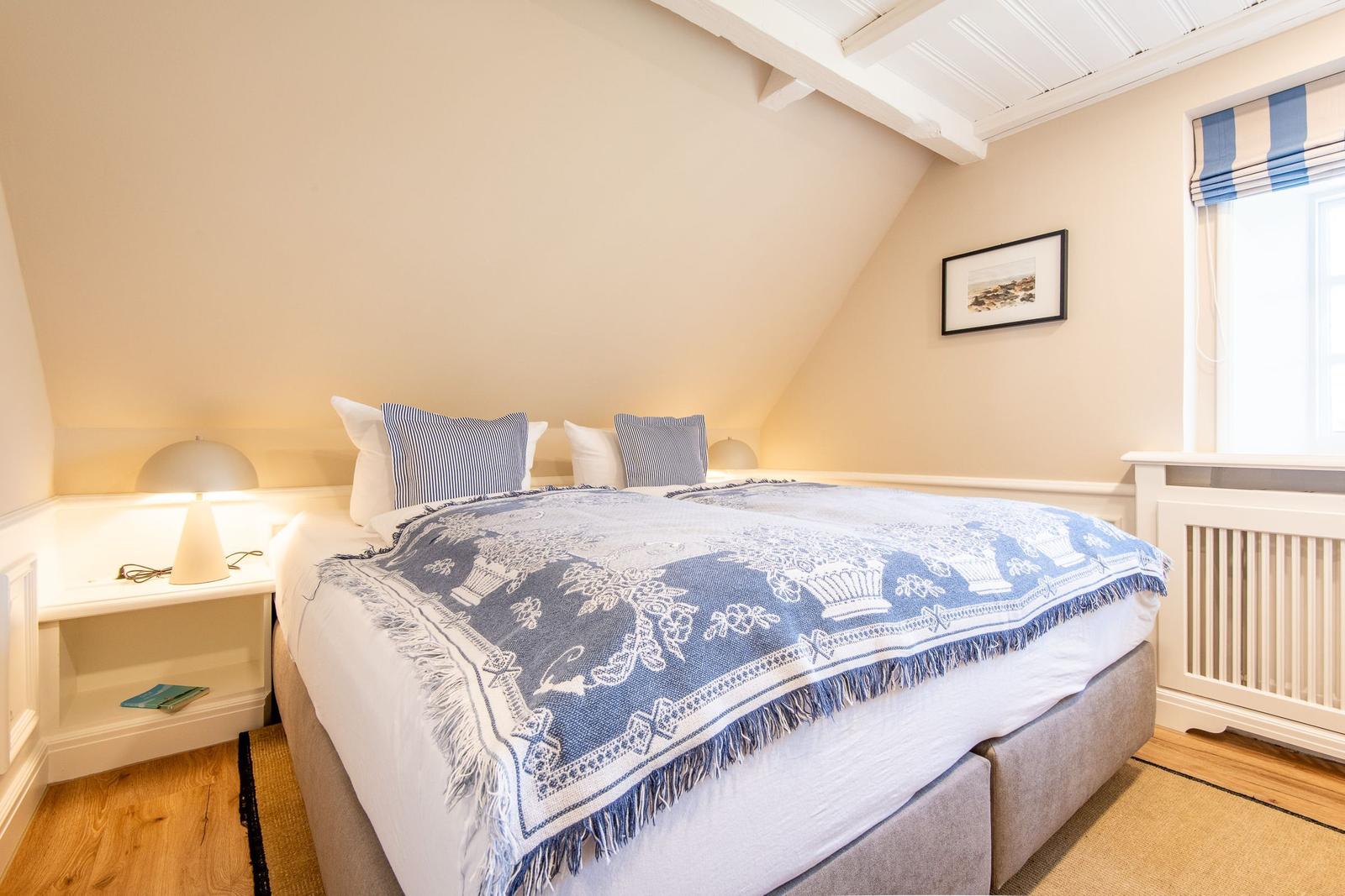 Schlafzimmer mit Dachschräge, Bett mit blau-weißem Deckenbezug und Fenster mit blau-weißem Rolladen.