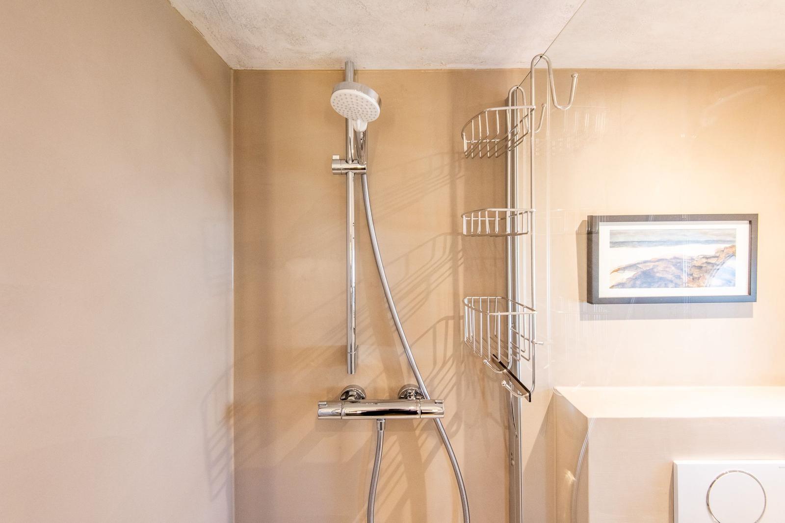 Dusche mit Duschbrause und Aufbewahrungskorb an der Wand
