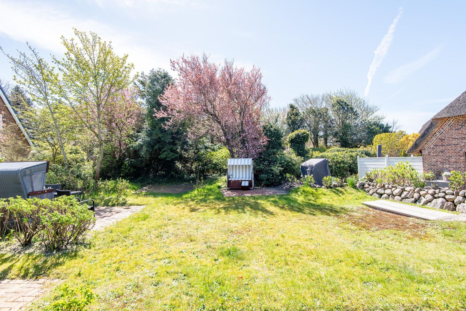 Grüner Garten mit Blumen, Bäumen und Gartenmöbeln. Hinterhof mit Steinmauer und Holzhaus.