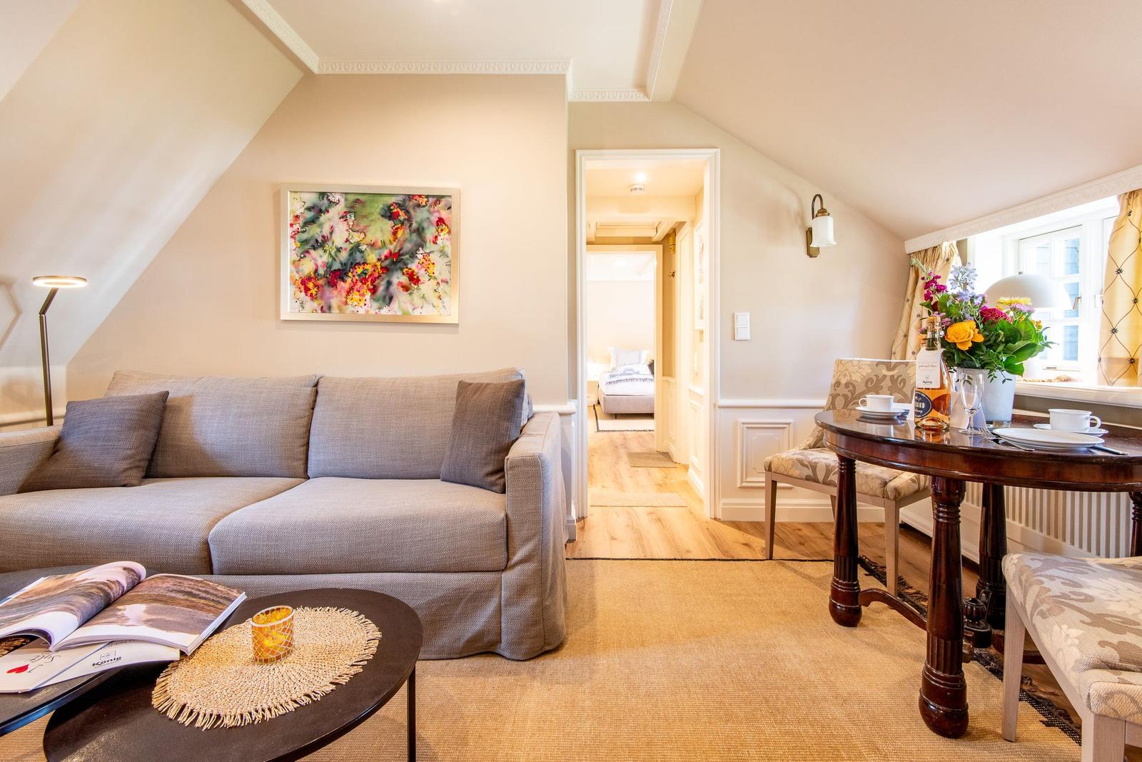 Wohn- und Essbereich mit Sofa, Tisch und Blick in Schlafzimmer.