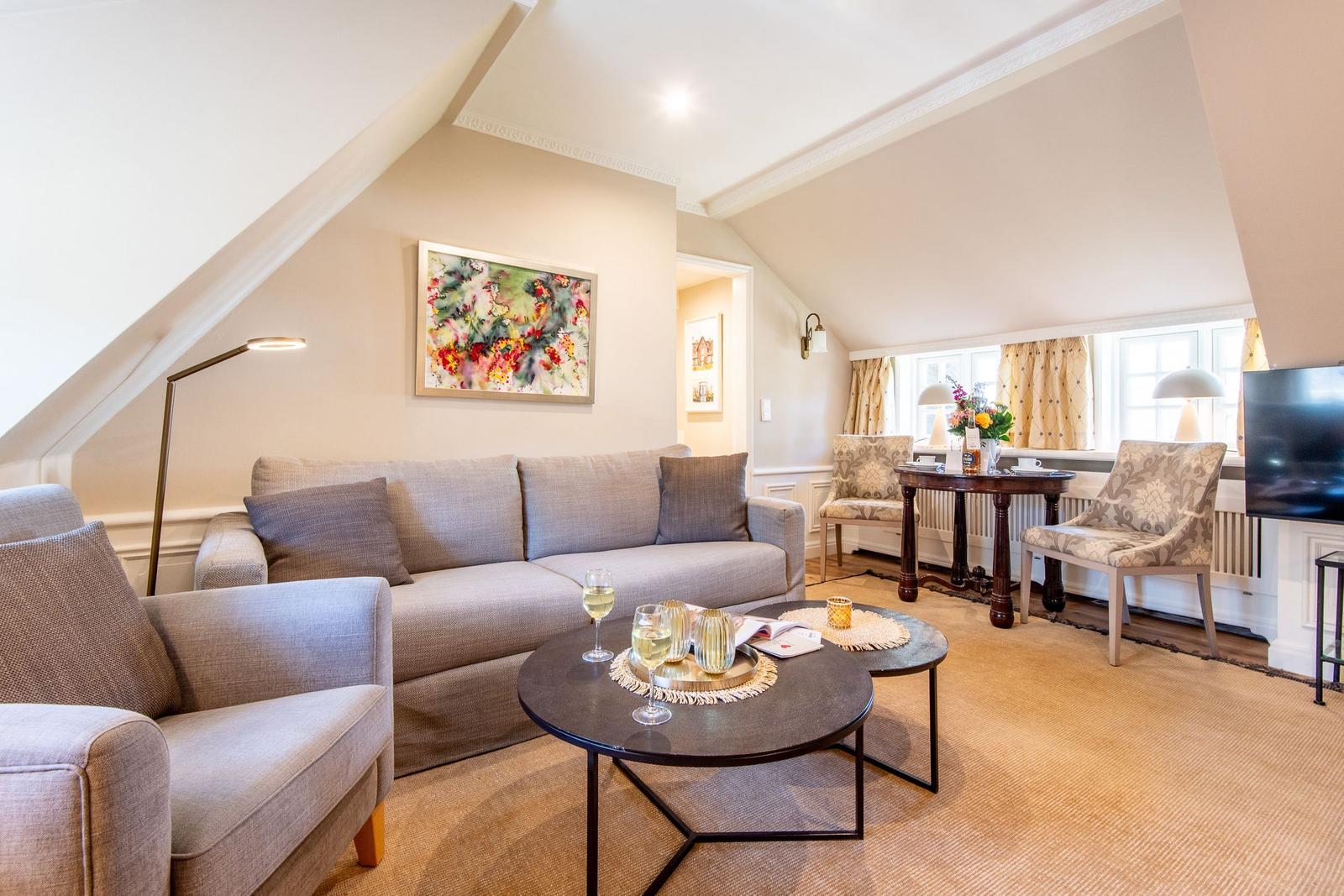 Wohnzimmer mit Sofa, Sessel und Tisch unter schrägen Dachschrägen.