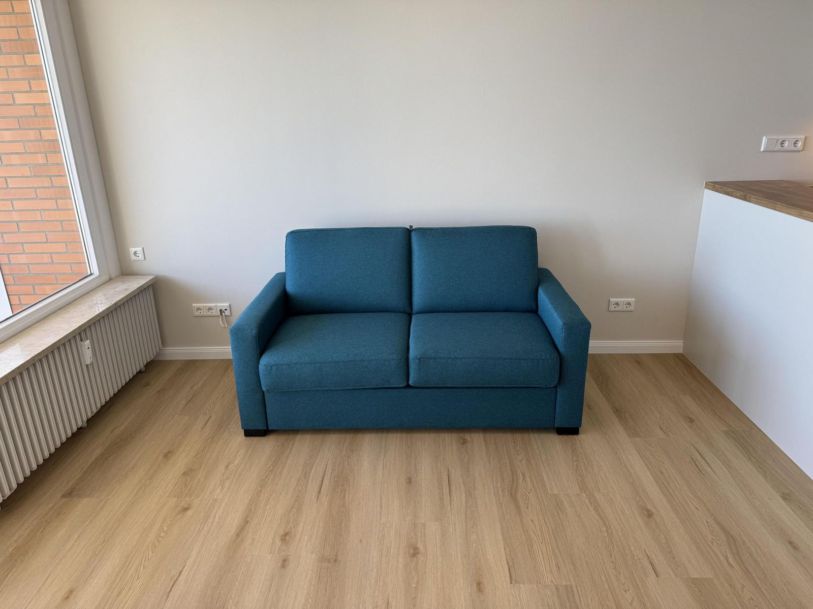 A blue sofa in the living room with wooden floor and window.