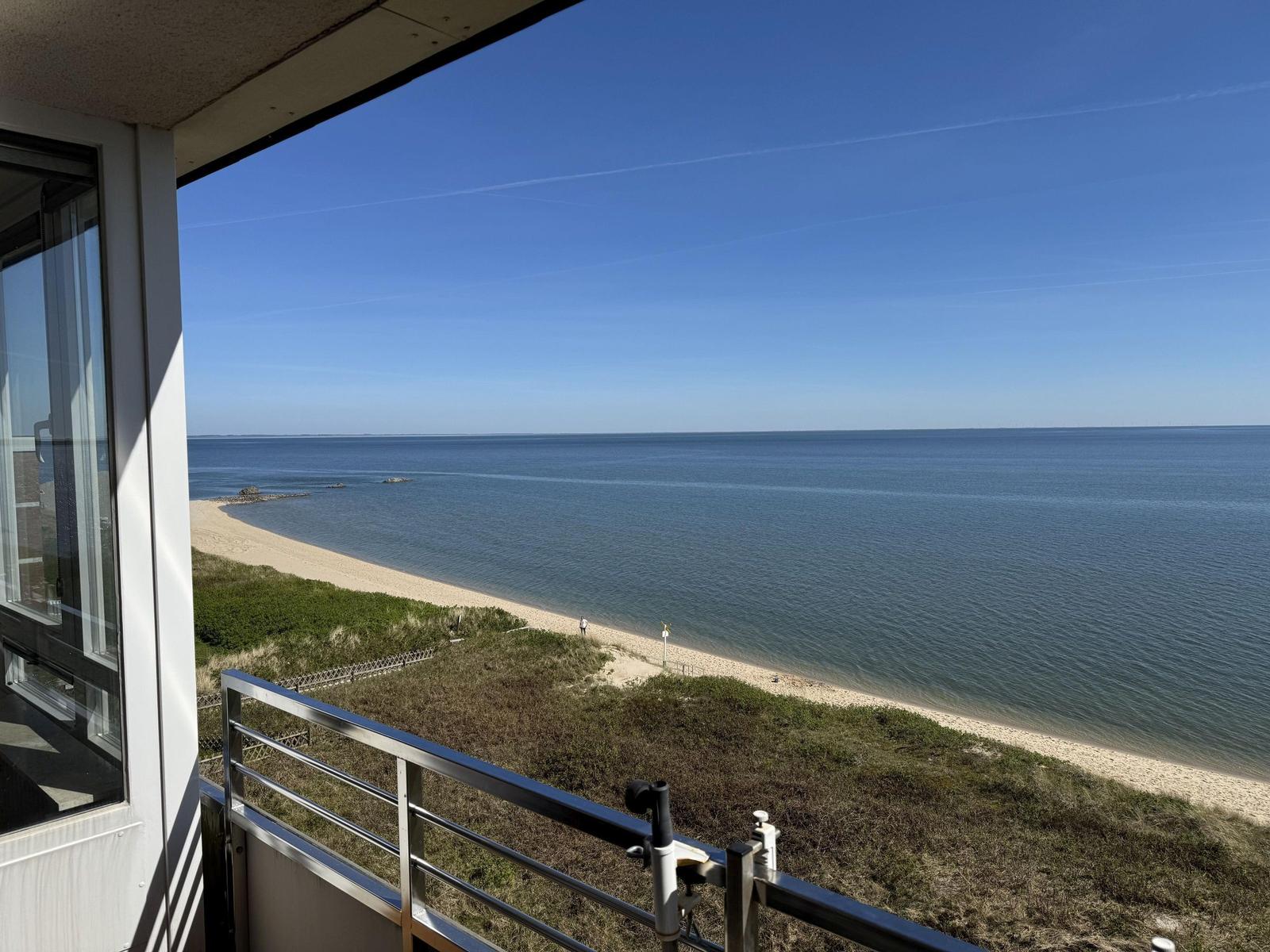 View from balcony over beach and sea under blue sky.