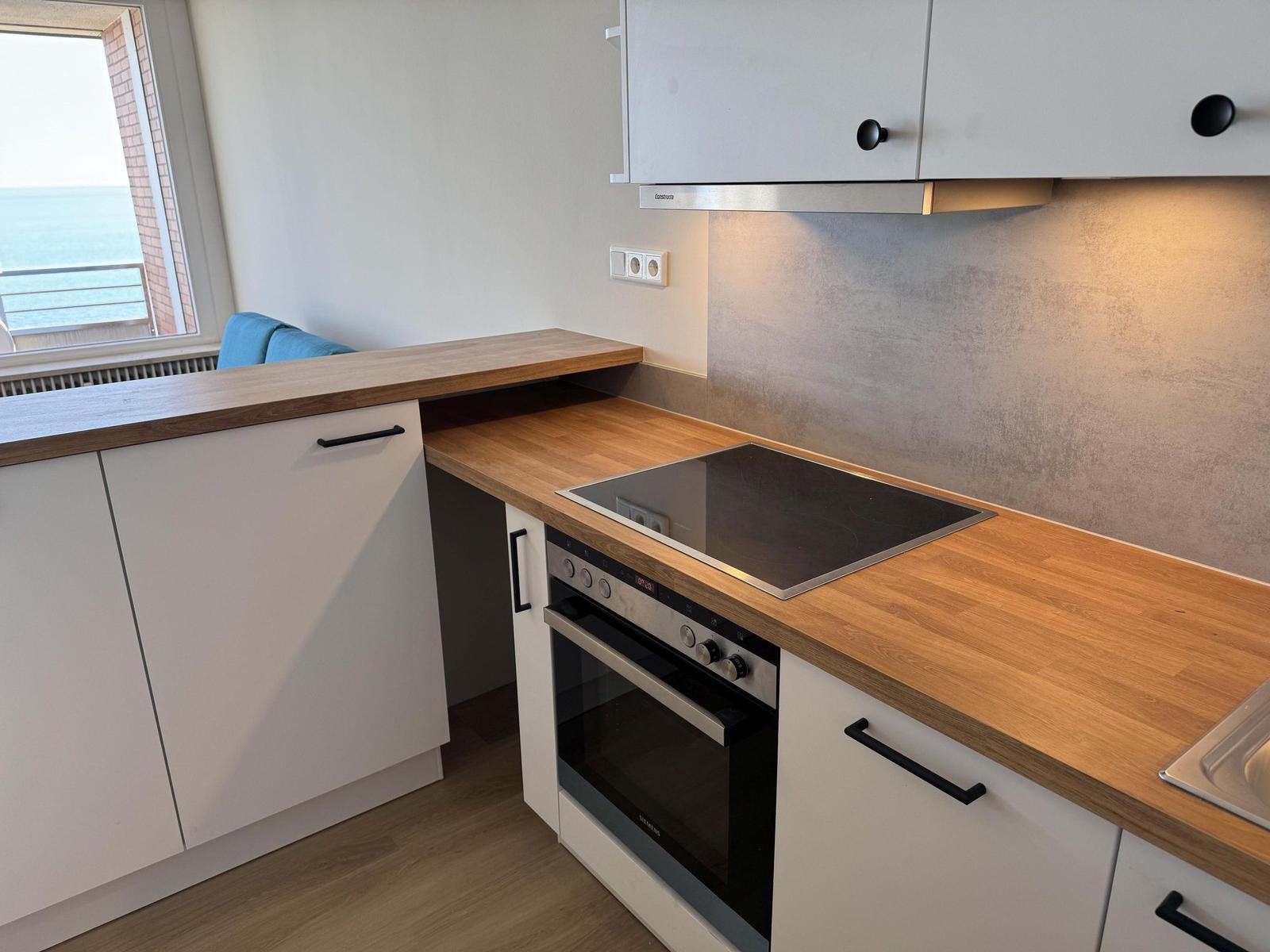 Kitchen with cooktop and oven, wooden worktop, window with sea view.