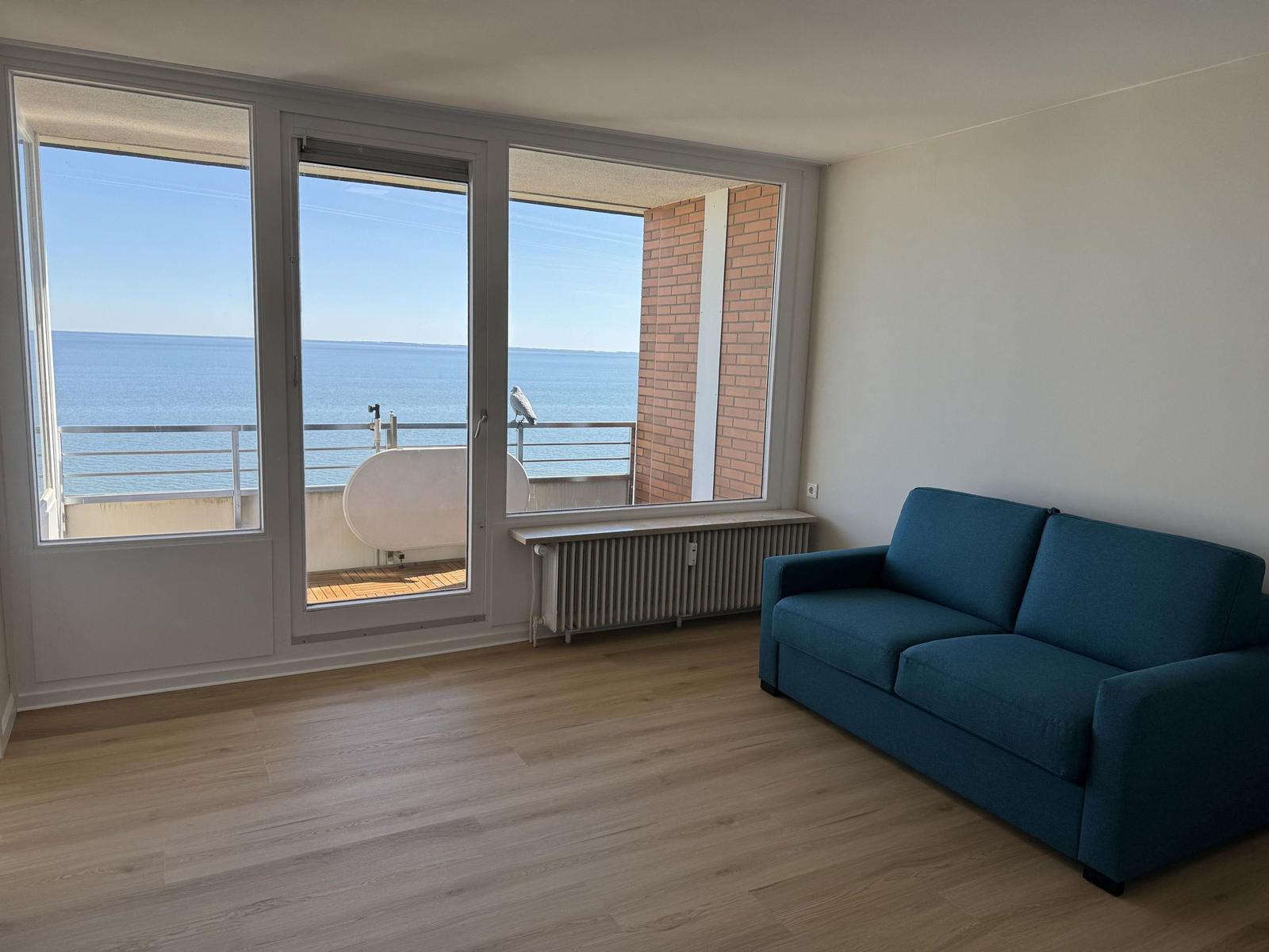 Living room with blue sofa and sea view through large windows.
