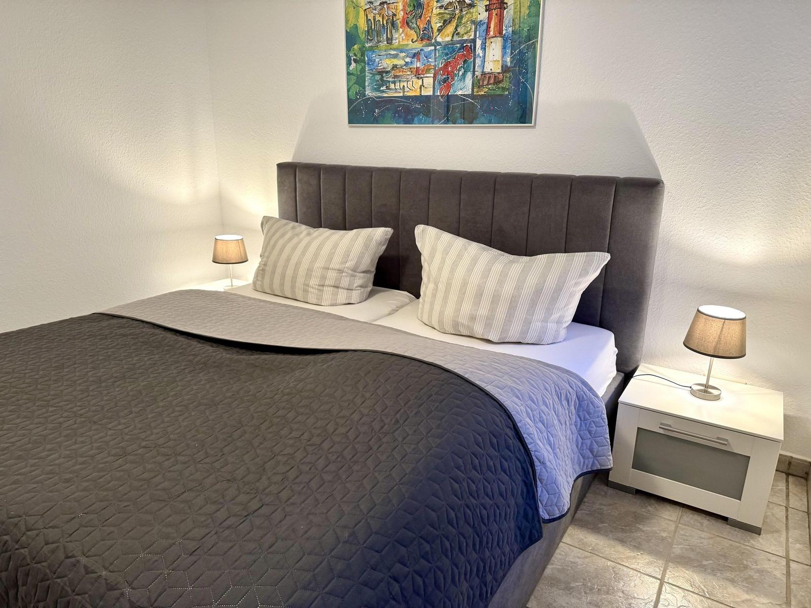 Schlafzimmer mit Bett, zwei Nachttischen und Wandbild.