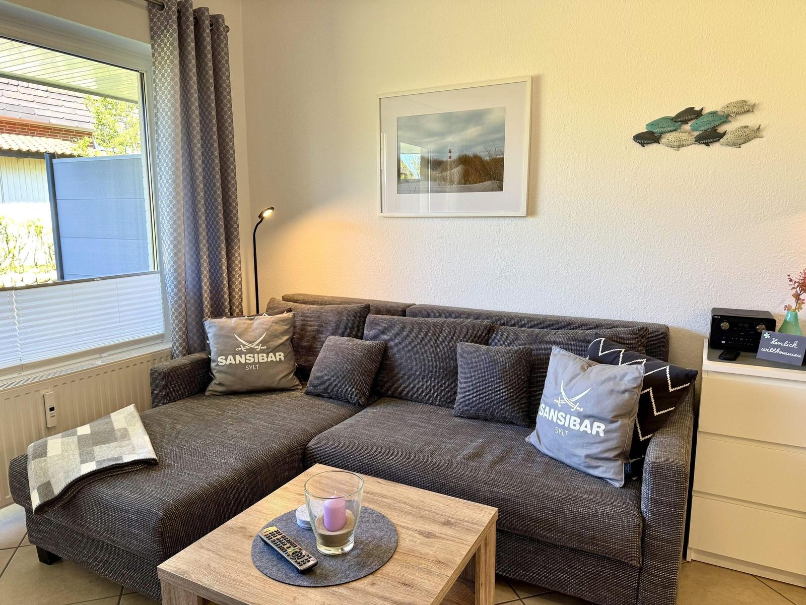 Ein Wohnzimmer mit grauem Sofa, Tisch und Fenster.