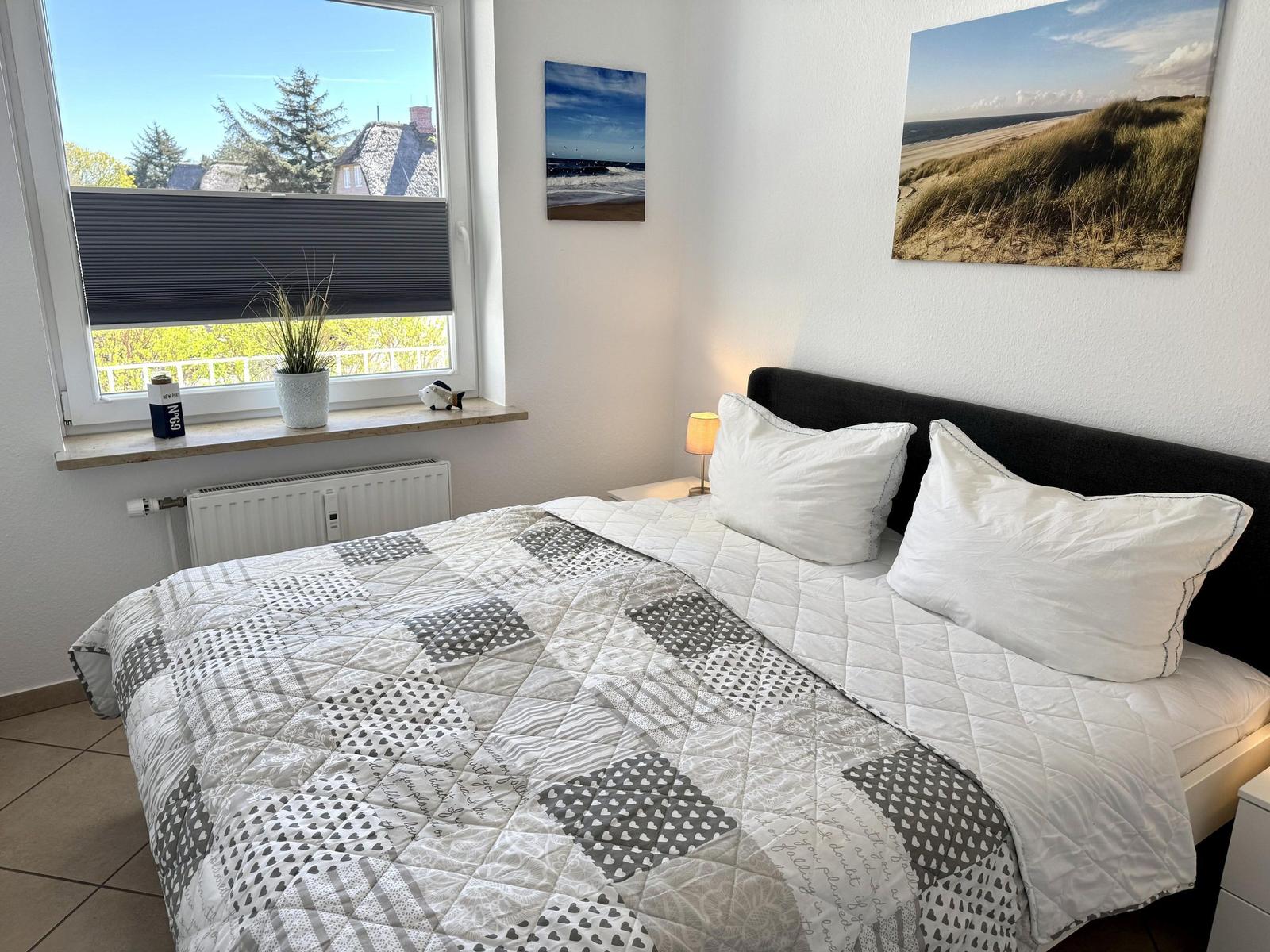 Schlafzimmer mit Bett, Fenster und Wandbildern.