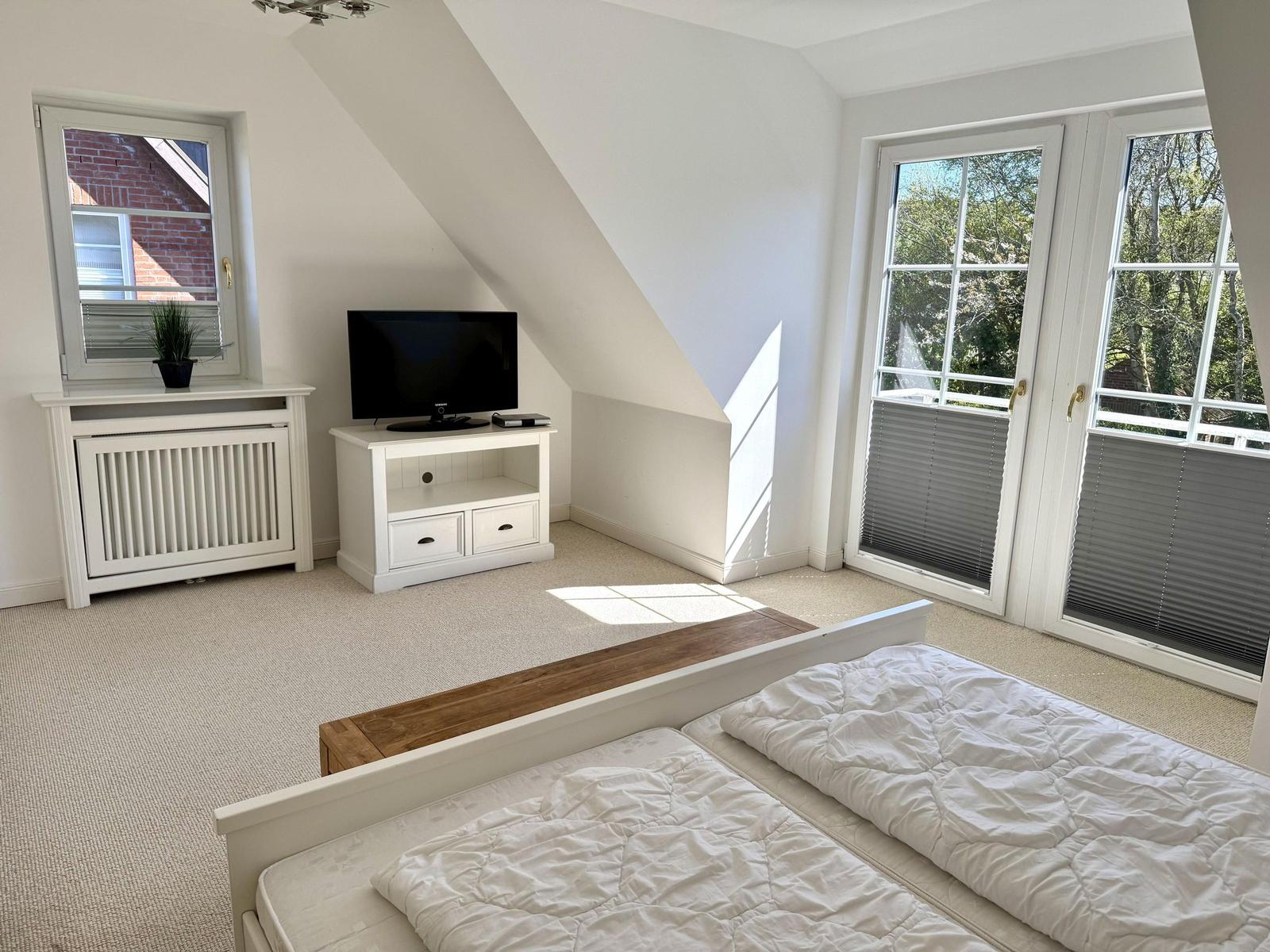 Schlafzimmer mit Dachschräge, TV und Balkontür.