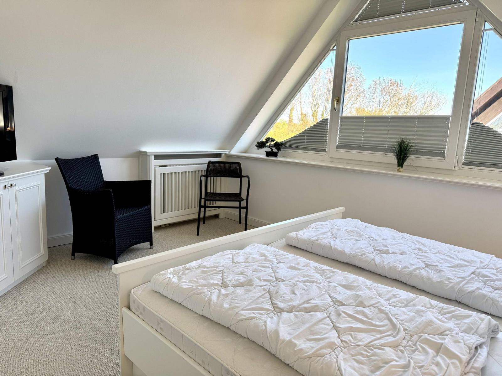 Zimmer mit Doppelbett, Fenster und Sitzgelegenheit.