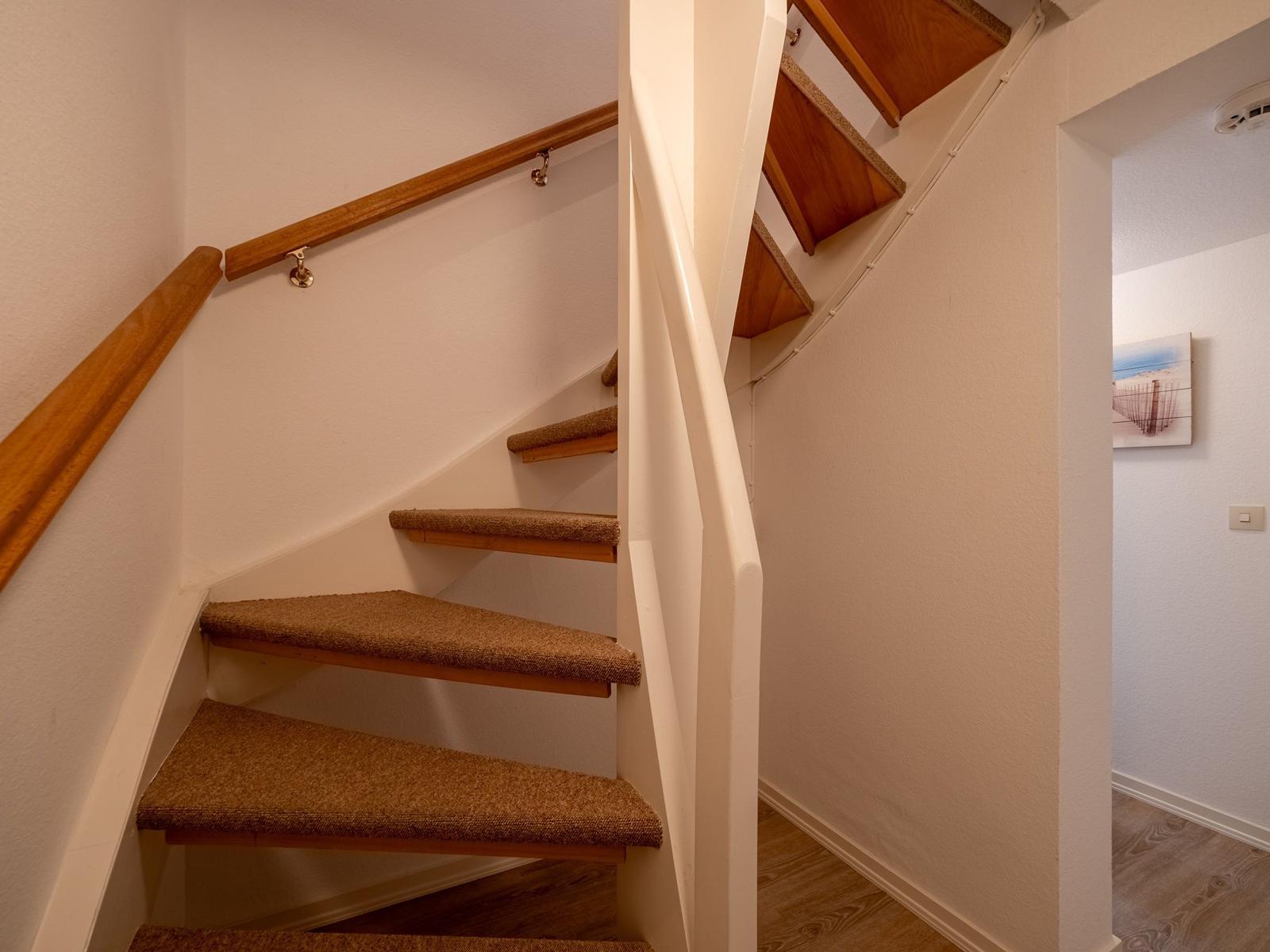 Treppenhaus mit Holzgeländer und Teppichstufen führt zur oberen Etage.