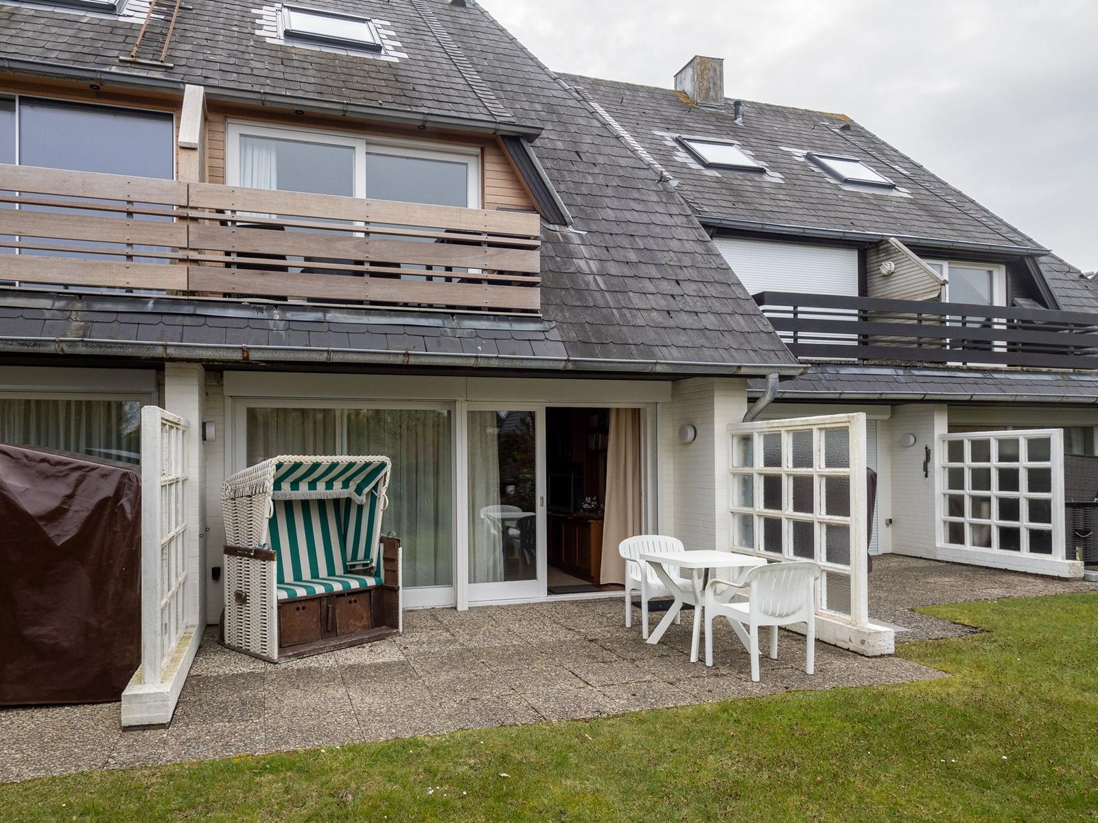 Terrasse mit Strandkorb und Tisch. Haus mit Balkon und Dachfenstern.