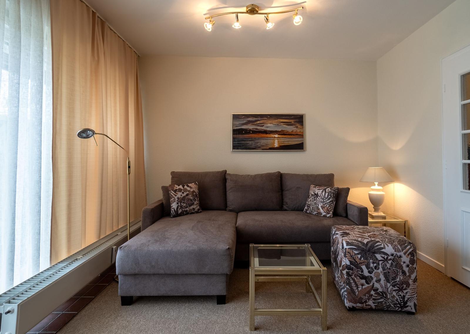 Ein Wohnzimmer mit grauem Sofa, Glas-Tisch und Beistelltisch.